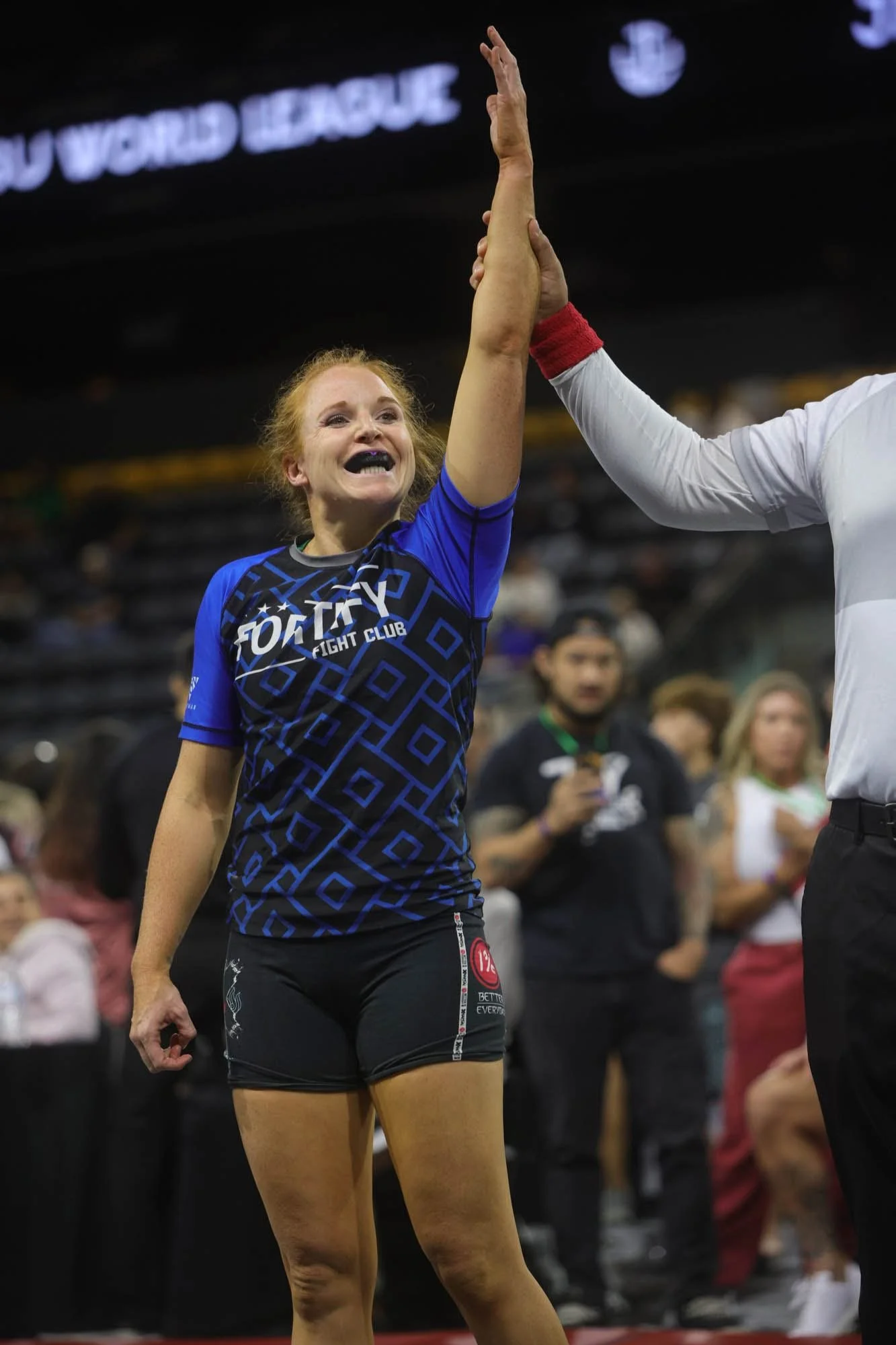 Female athlete with red hair in athletic attire high-fiving a person in a white shirt at a sports event indoor stadium