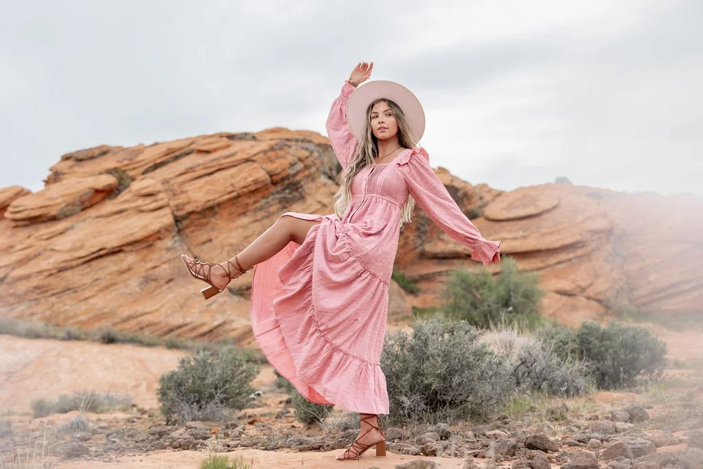 Editorial fashion photography in Southern Utah featuring a female model in a flowing pink dress against the dramatic red rock desert landscape. This creative fashion photoshoot blends movement, styling, and natural scenery to create striking campaign