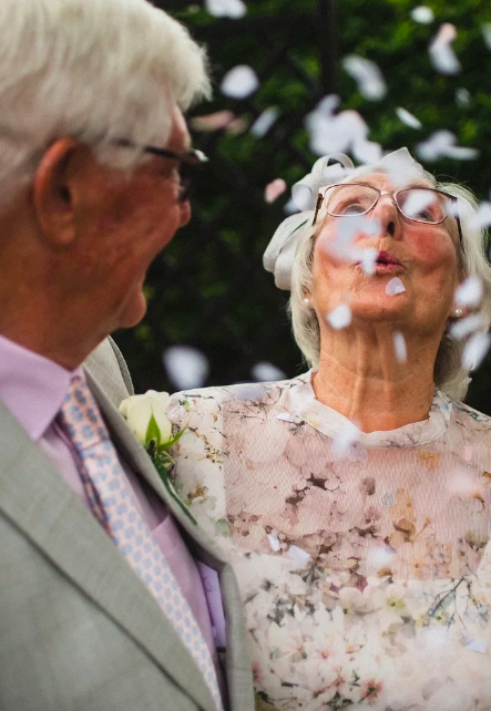 Un couple habillé élégamment s'embrasse sous un arbre dans un parc.