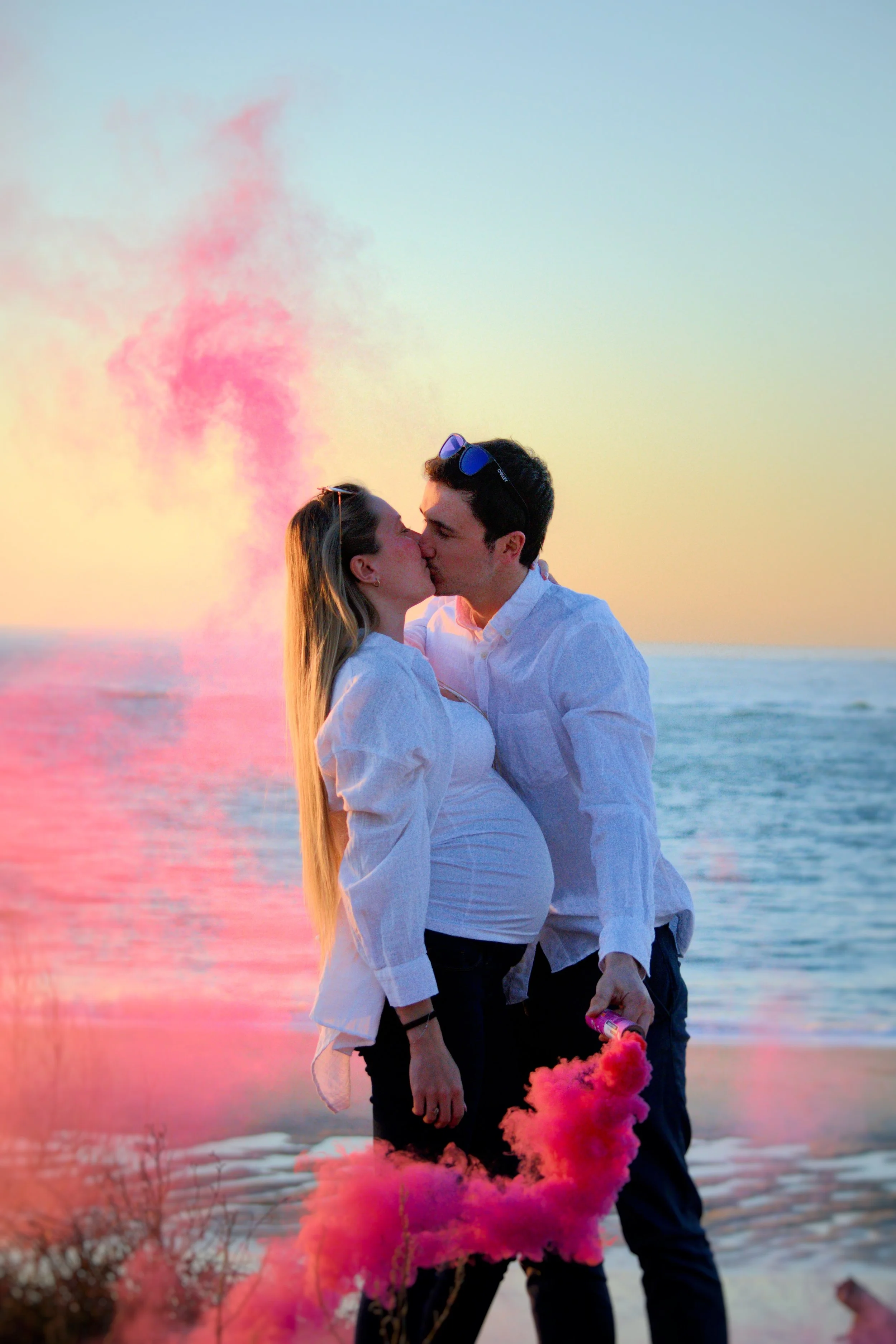 Couple s'embrassant sur la plage au coucher du soleil avec fumée rose en arrière-plan.