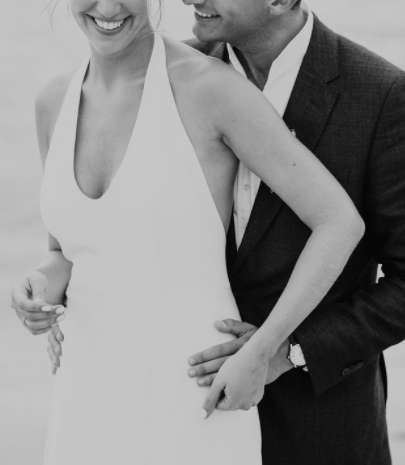 Un couple habillé de manière élégante, avec une femme en robe de mariée et un homme en costume, partage un moment intime et joyeux.