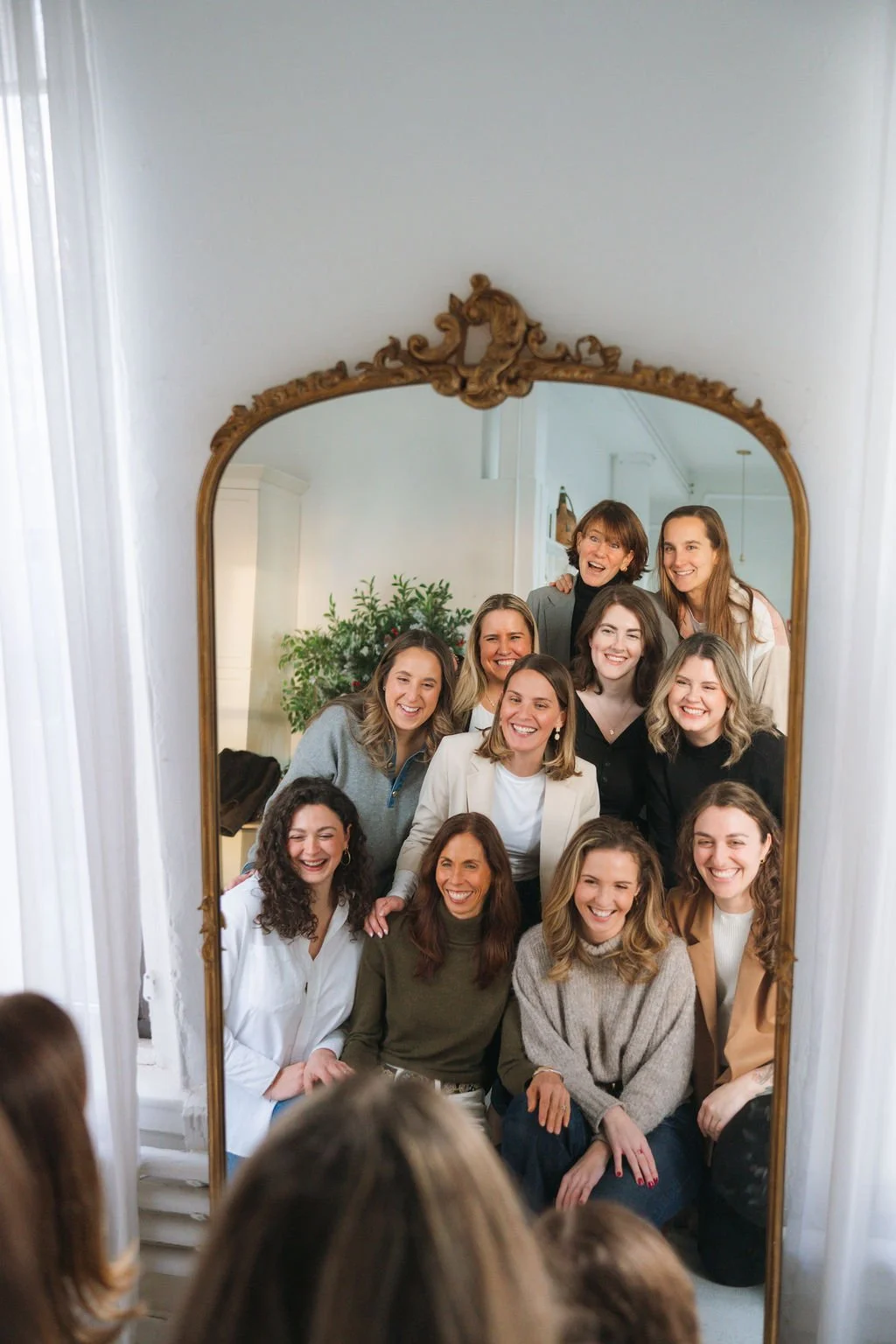 A group of women smiling and posing together for a photo in front of a large ornate mirror.