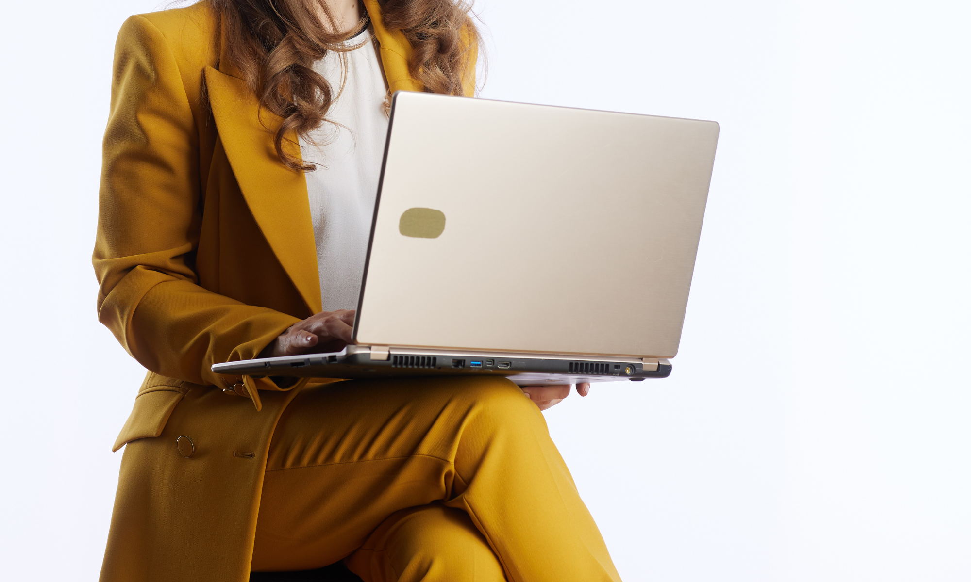 A woman wearing a yellow suit sitting and working on a silver laptop.