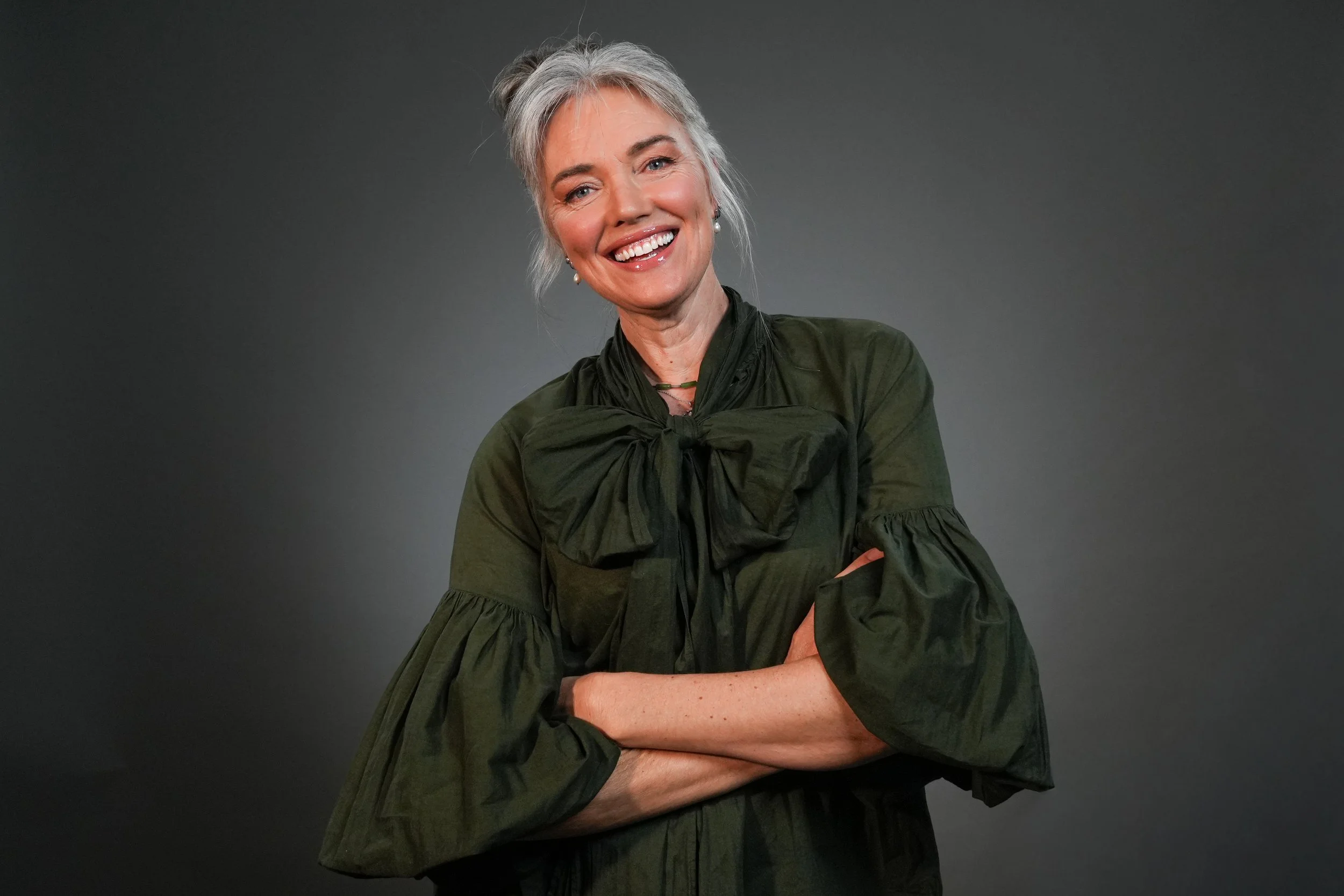 Smiling woman with gray hair wearing a striped shirt against a plain background.