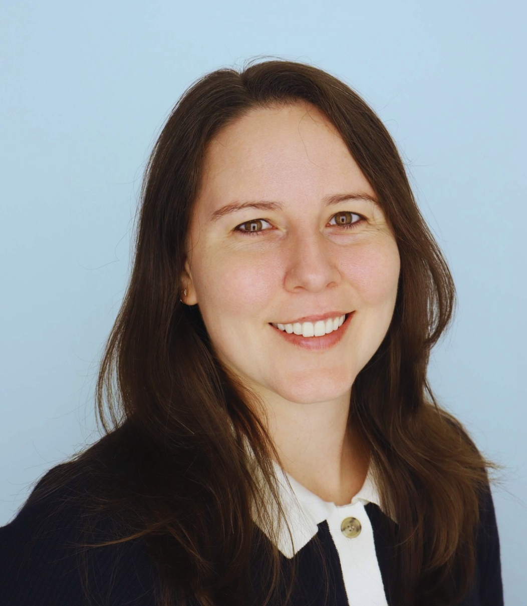 A woman with long brown hair smiling, set against a light blue background.