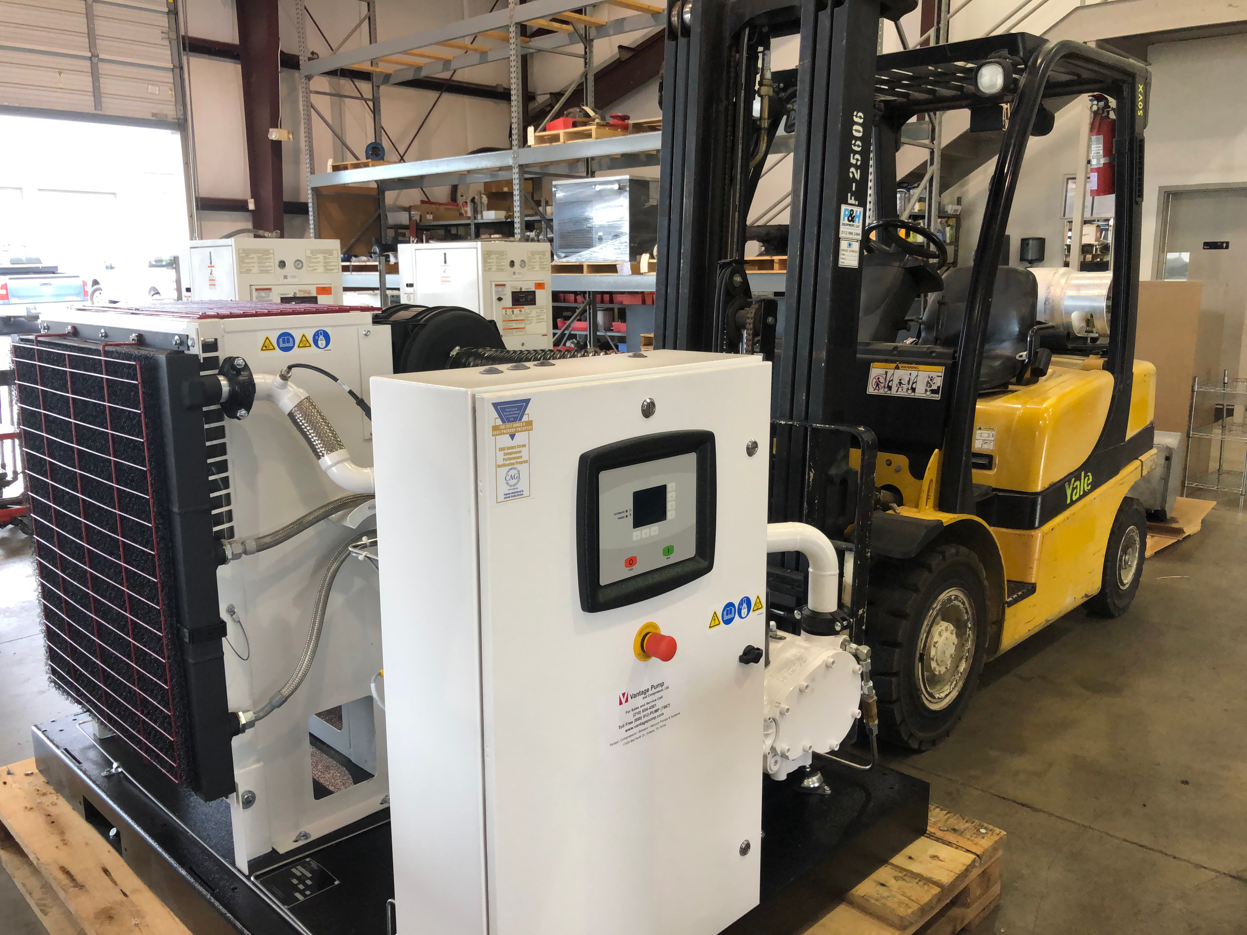 A yellow Yale forklift located inside a warehouse next to an industrial cooling or refrigeration unit with a control panel, pipes, and a radiator.