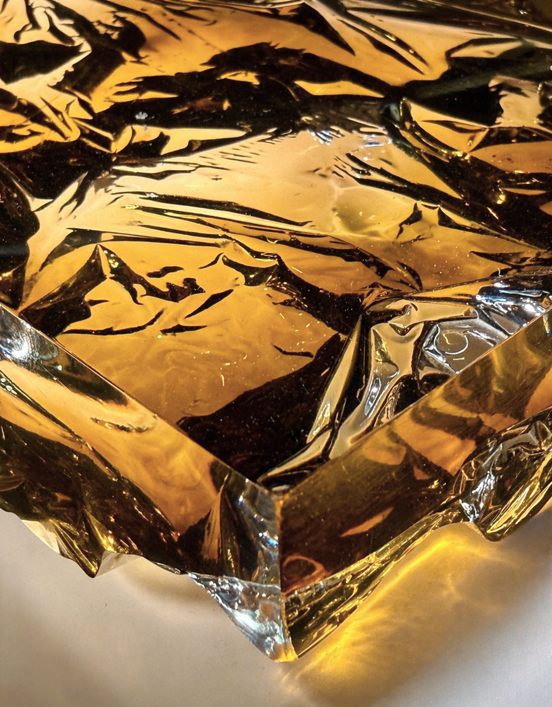 Translucent cast resin panel in warm amber, smoke, and gold tones with subtle metallic reflections, featuring a textured back that refracts light and creates a glowing, layered effect.