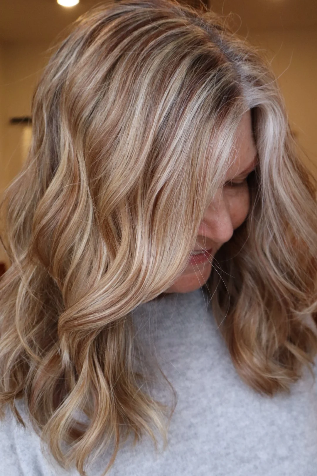 Close-up of a woman with long, blonde, wavy hair smiling and looking down.