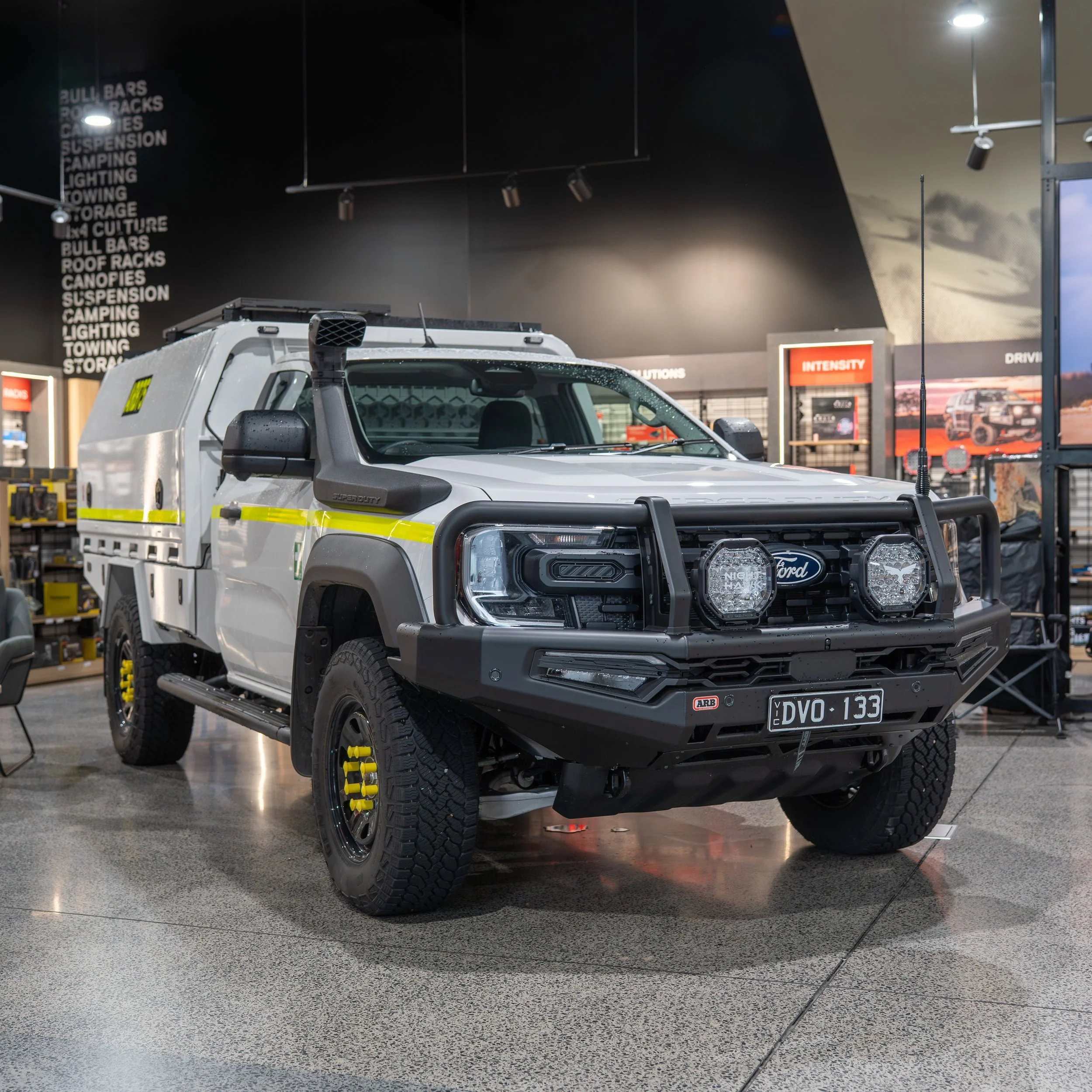 A white Ford Ranger Superduty with off-road tires and a black front grille, equipped for work, inside a store that sells outdoor and camping equipment.