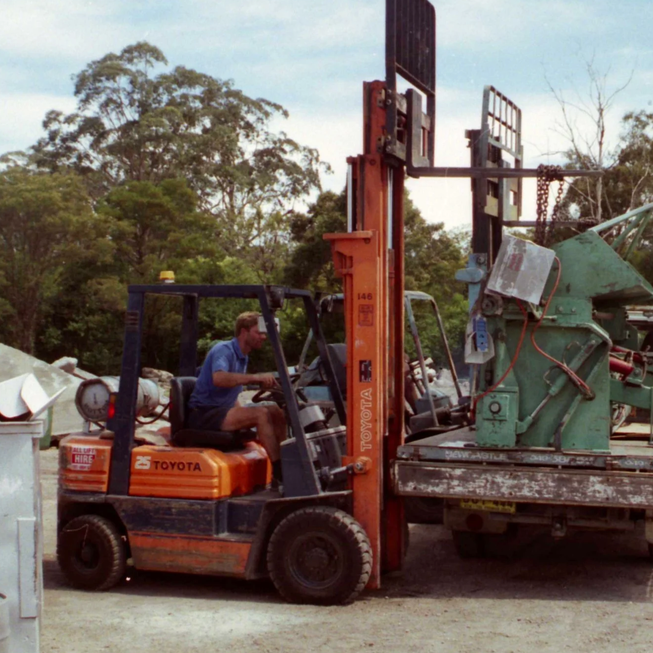 Man operating a forklift on a construction site surrounded by trees and equipment.