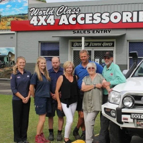 Group of six people standing in front of a 4x4 accessory store and a vehicle.
