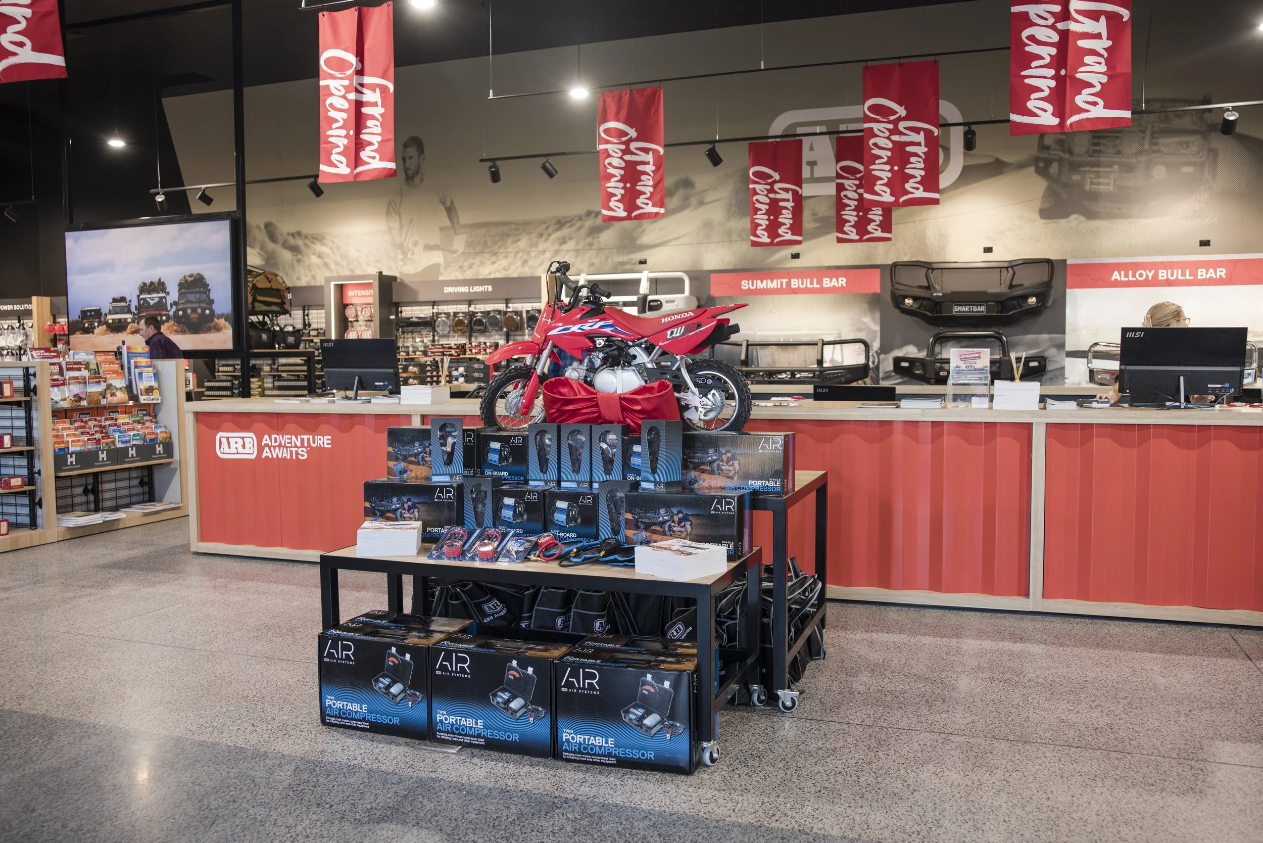 Store interior with a red motorcycle displayed on a counter, surrounded by various auto accessories and equipment for off-road driving, with promotional banners hanging from the ceiling.