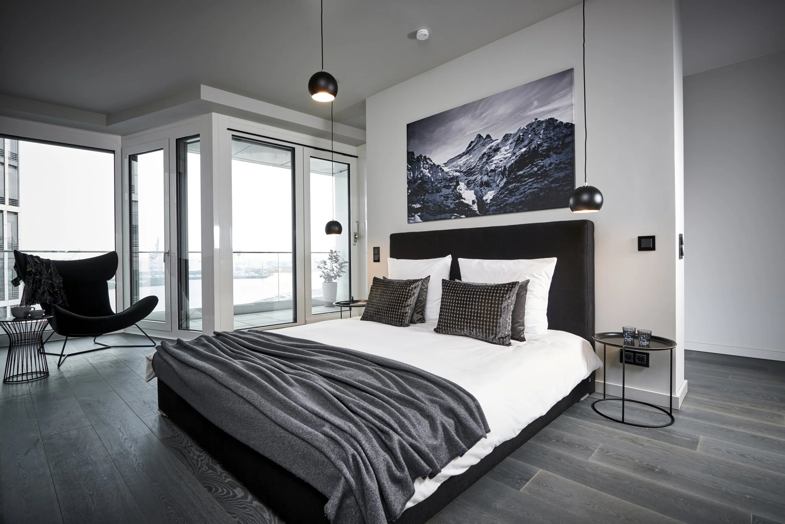 Schlafzimmer Penthouse Bett dunkelgrau Sessel Beistelltische BoConcept Fotokunst Pendelleuchten schwarz