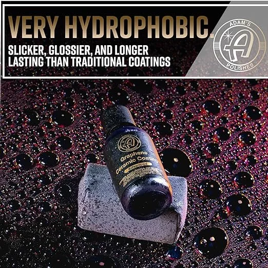 Bottle of Adam's Graphene Ceramic Coating resting on a foam block, surrounded by soap bubbles and vibrant water droplets on a black textured surface