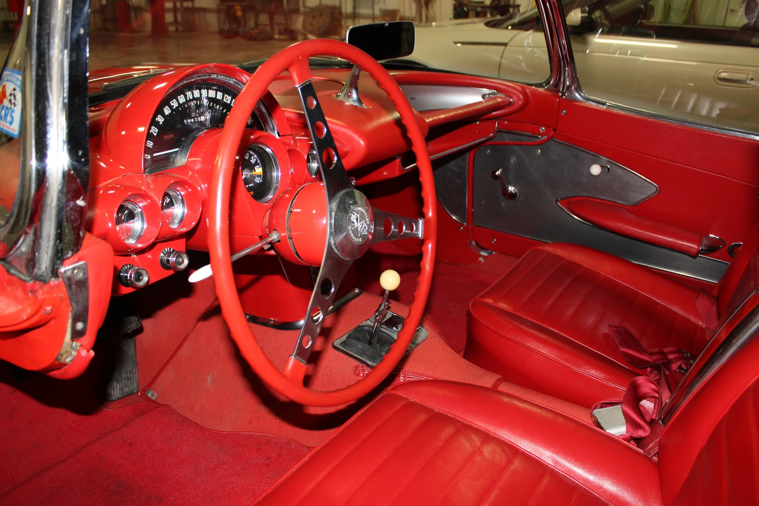 Interior of a vintage red car showing the dashboard, steering wheel, gear shift, and red leather seats.