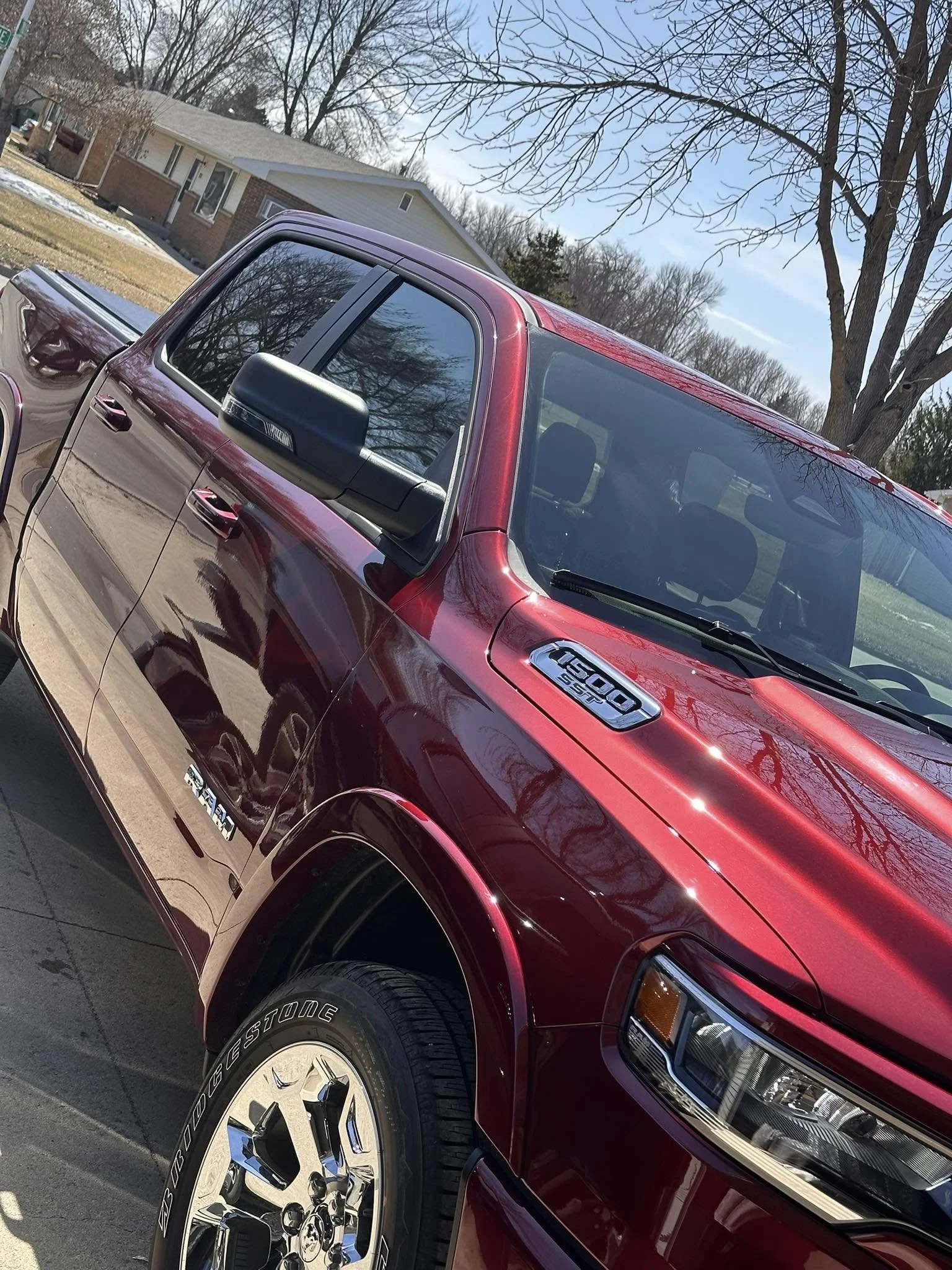A red Ram 1500 pickup truck parked outdoors on a sunny day, with a house and trees in the background.