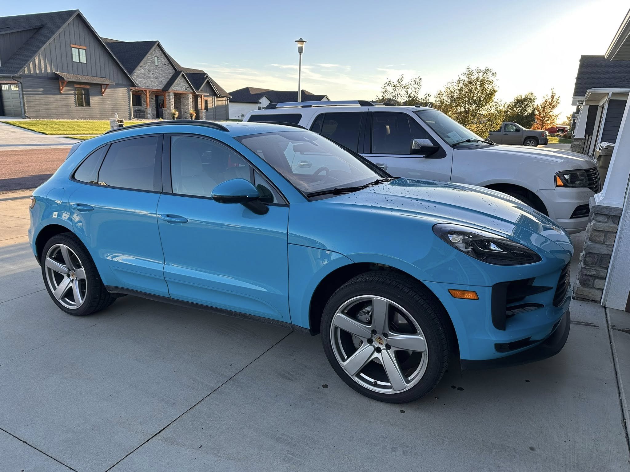 A blue hatchback car parked in a driveway with a silver SUV parked behind it, in a suburban neighborhood during daylight hours.
