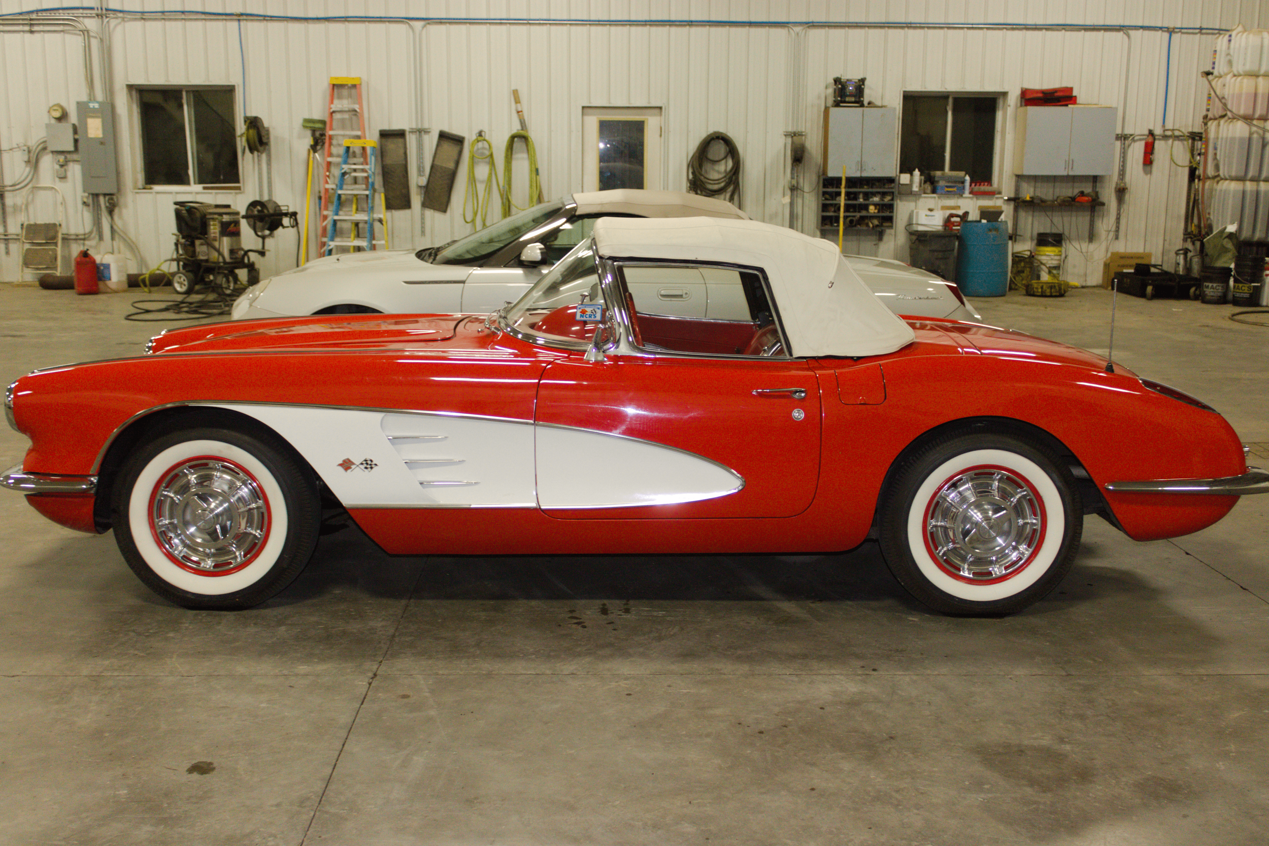 A red and white vintage Chevrolet Corvette convertible inside a garage.