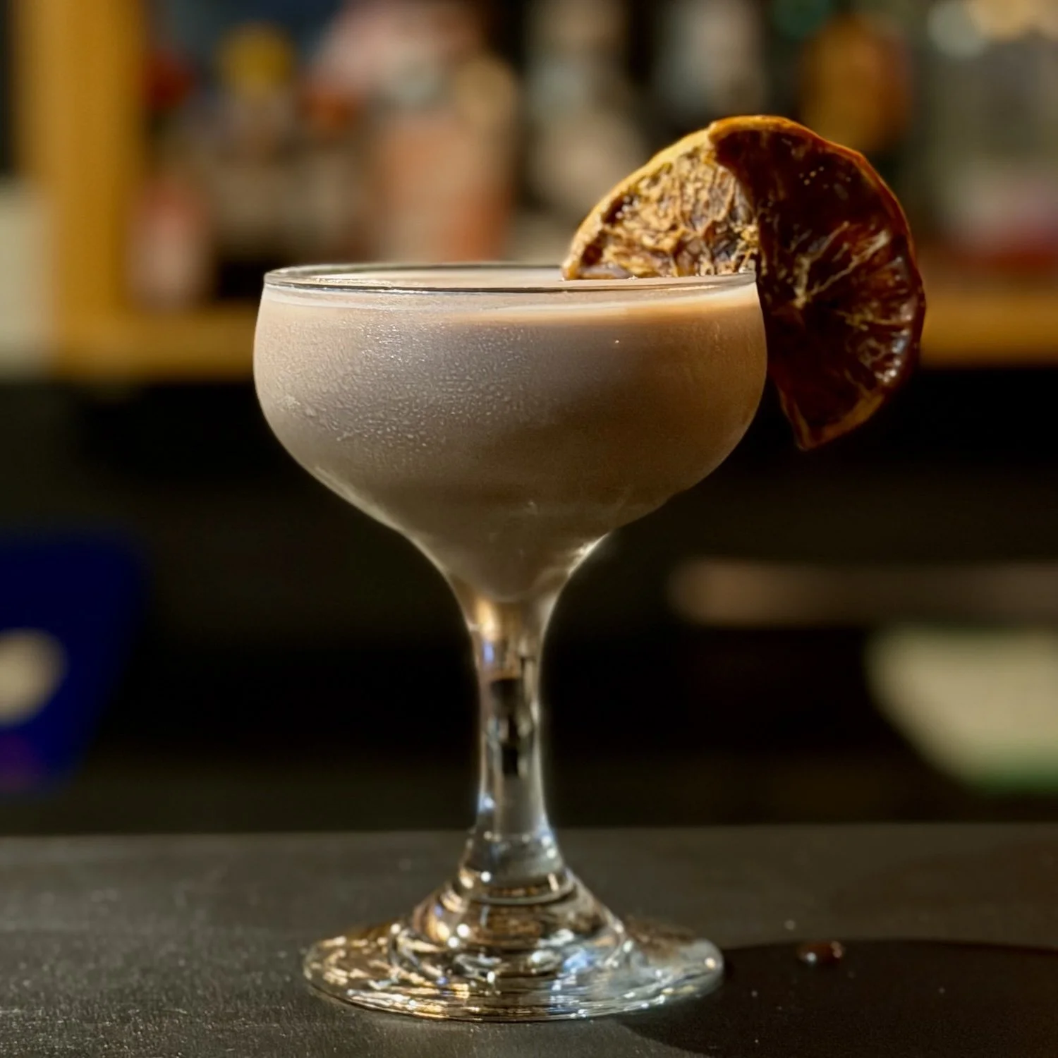 A cocktail in a coupe glass garnished with a dried citrus wheel.