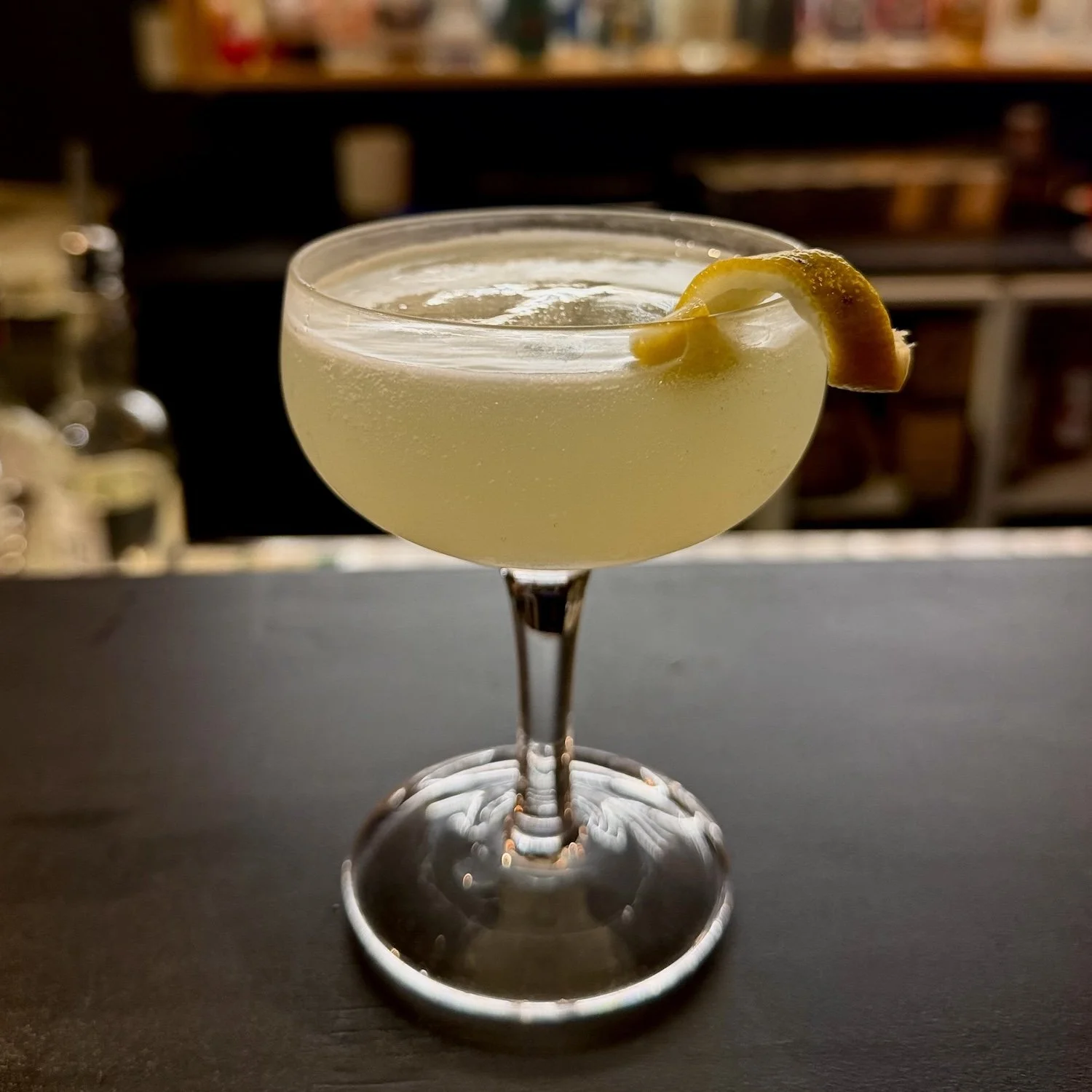 A cocktail in a coupe glass garnished with a lemon twist.