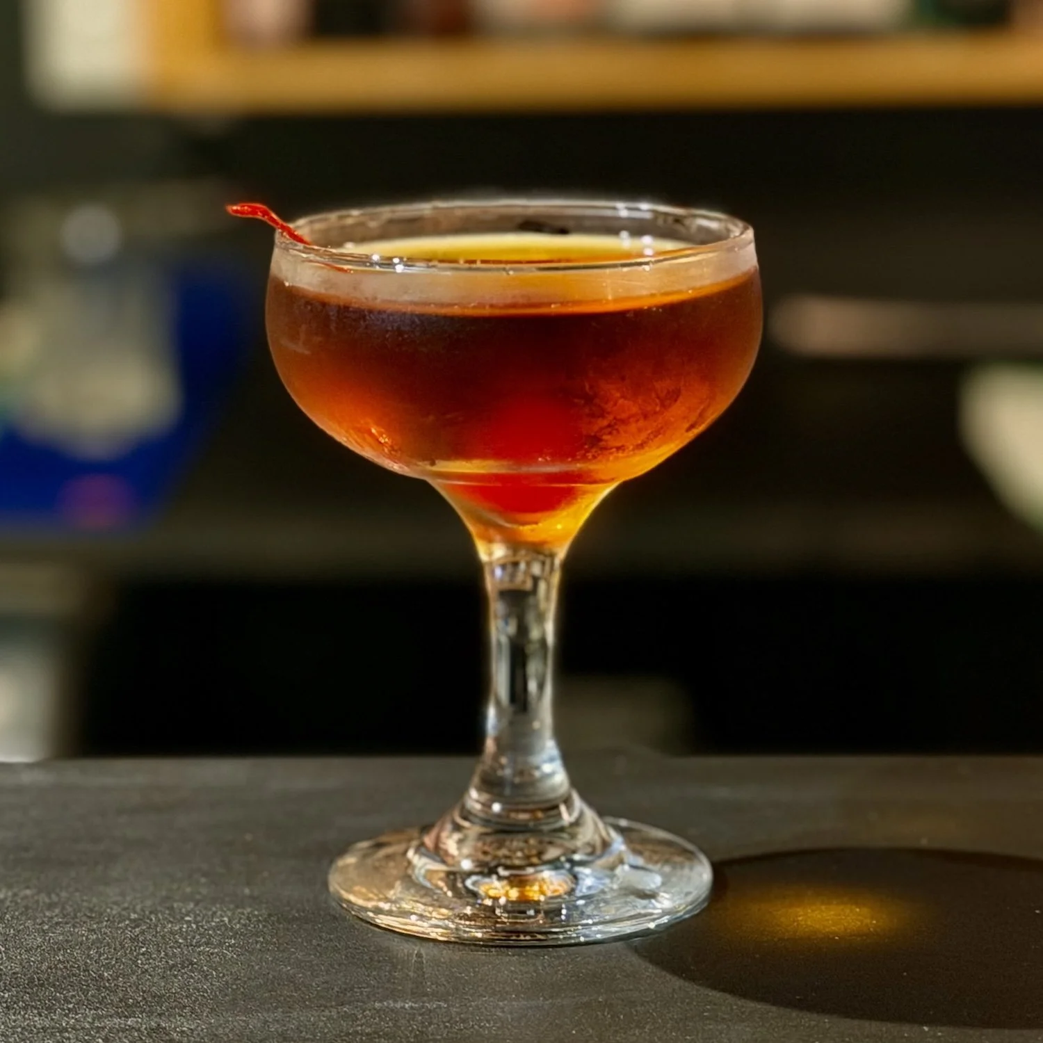 A coupe glass filled with a dark red cocktail with a cherry garnish.