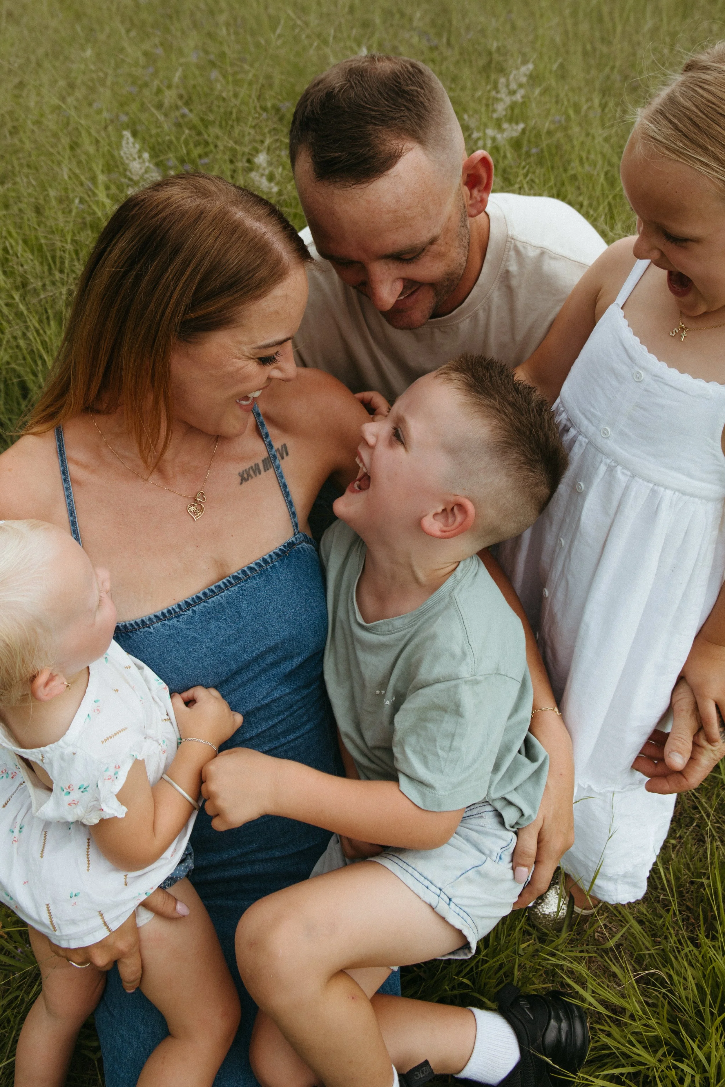 A family of five enjoying a joyful moment outdoors in a grassy field, smiling and laughing together.