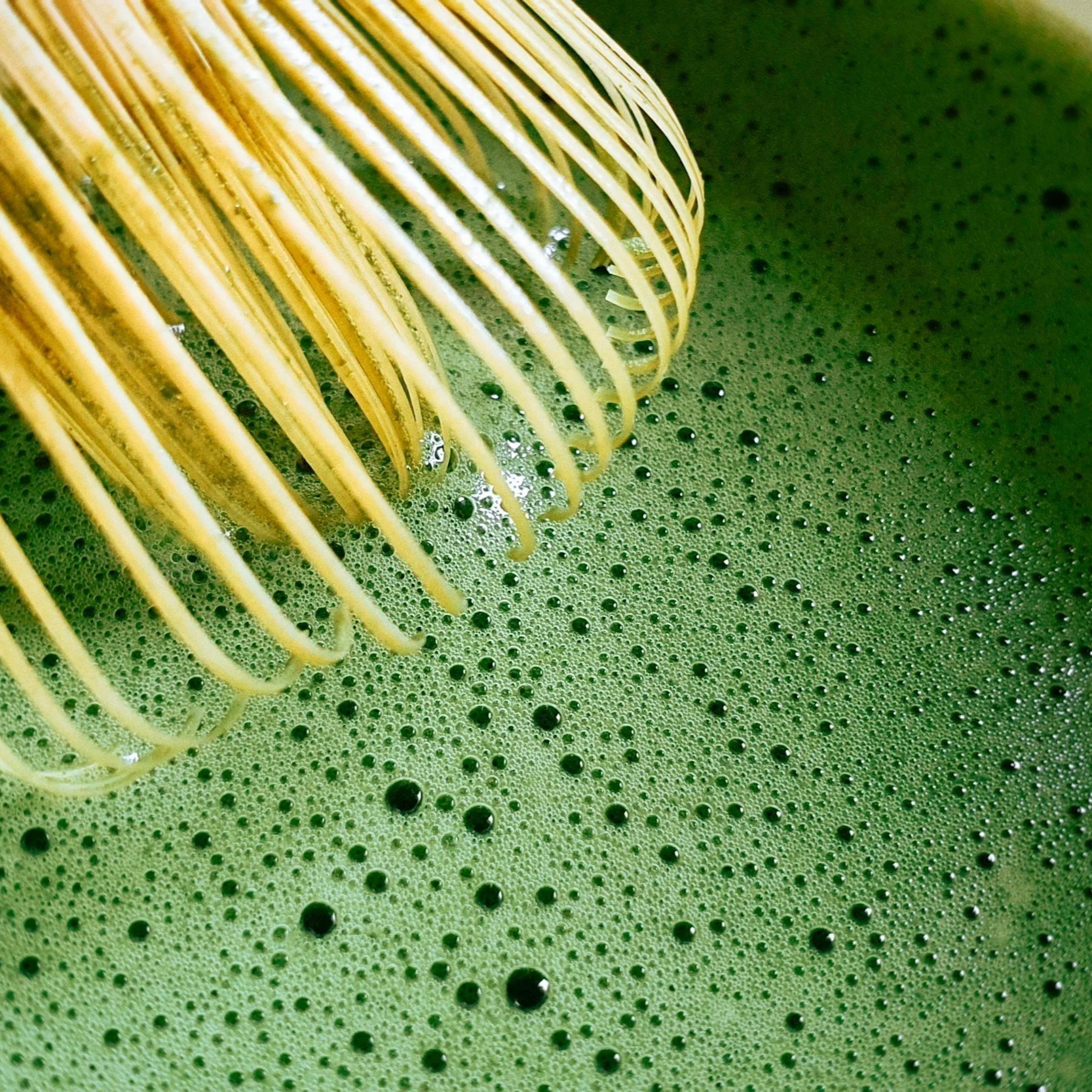 Close-up of whisked matcha foam with a bamboo whisk