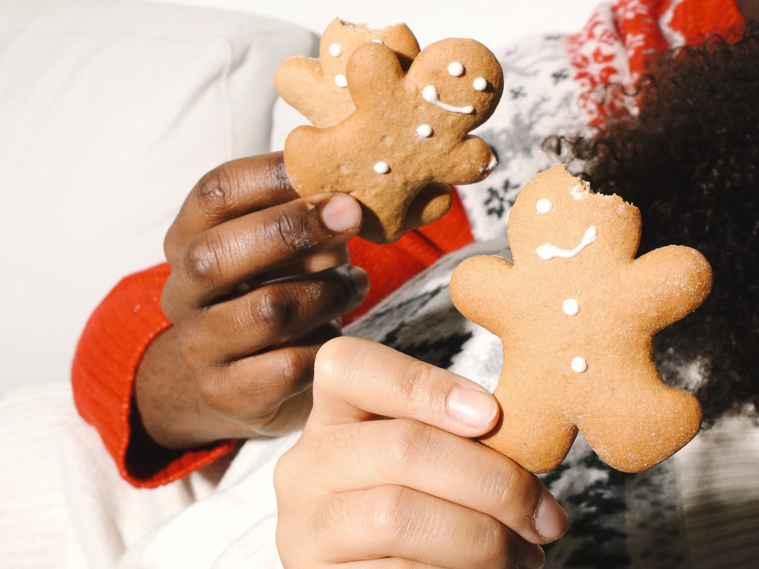 Two persons in festive holiday sweaters holding sugar-free gingerbread cookies