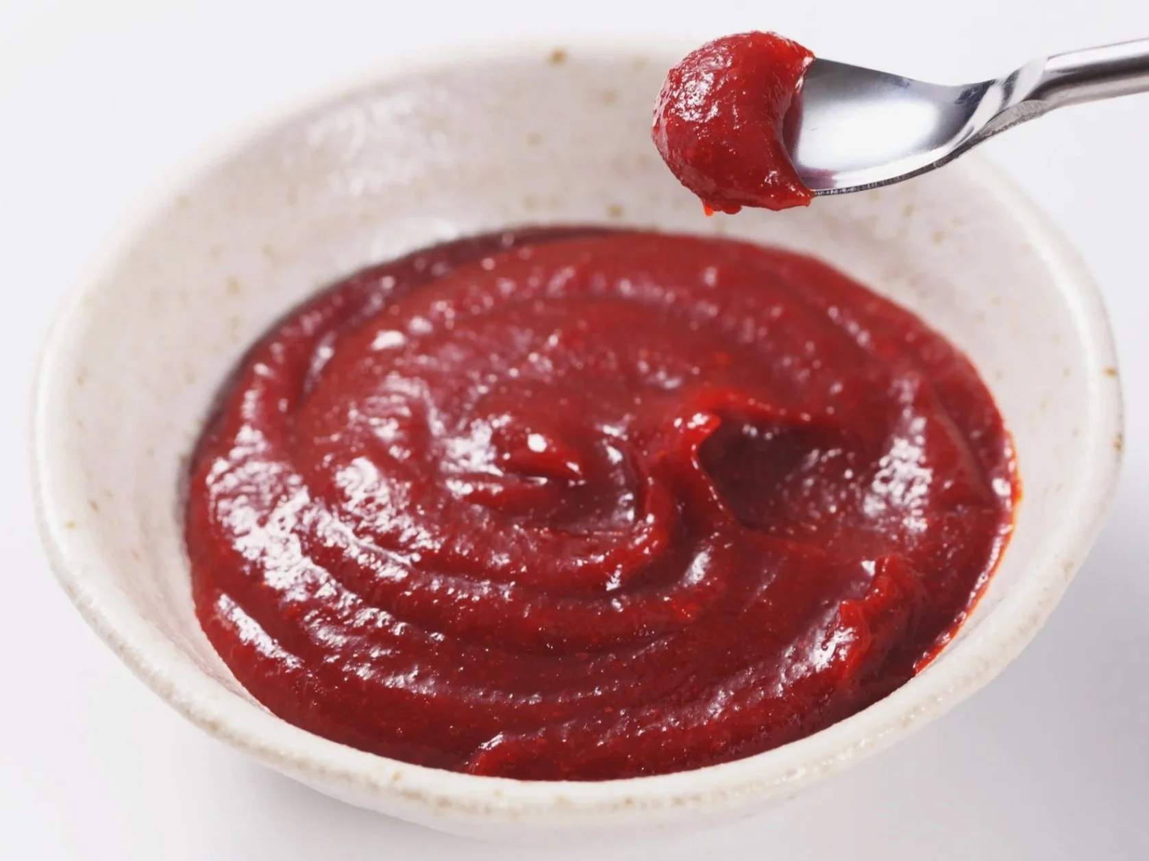 A ceramic bowl with barbecue sauce and a spoon