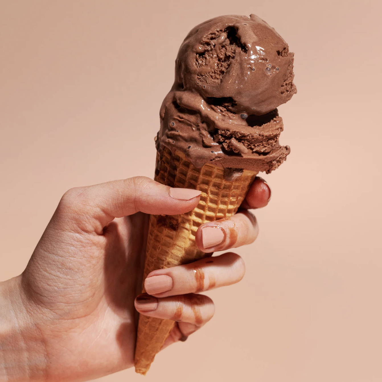 Melting chocolate ice cream cone held against a beige background