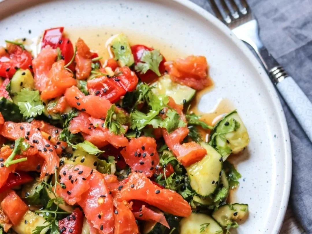 Smashed cucumber salad with smoked salmon and black sesame seeds in a plate with fork