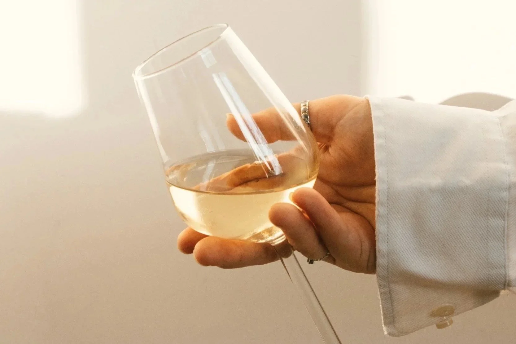 Woman holding glass of white wine beige aesthetic
