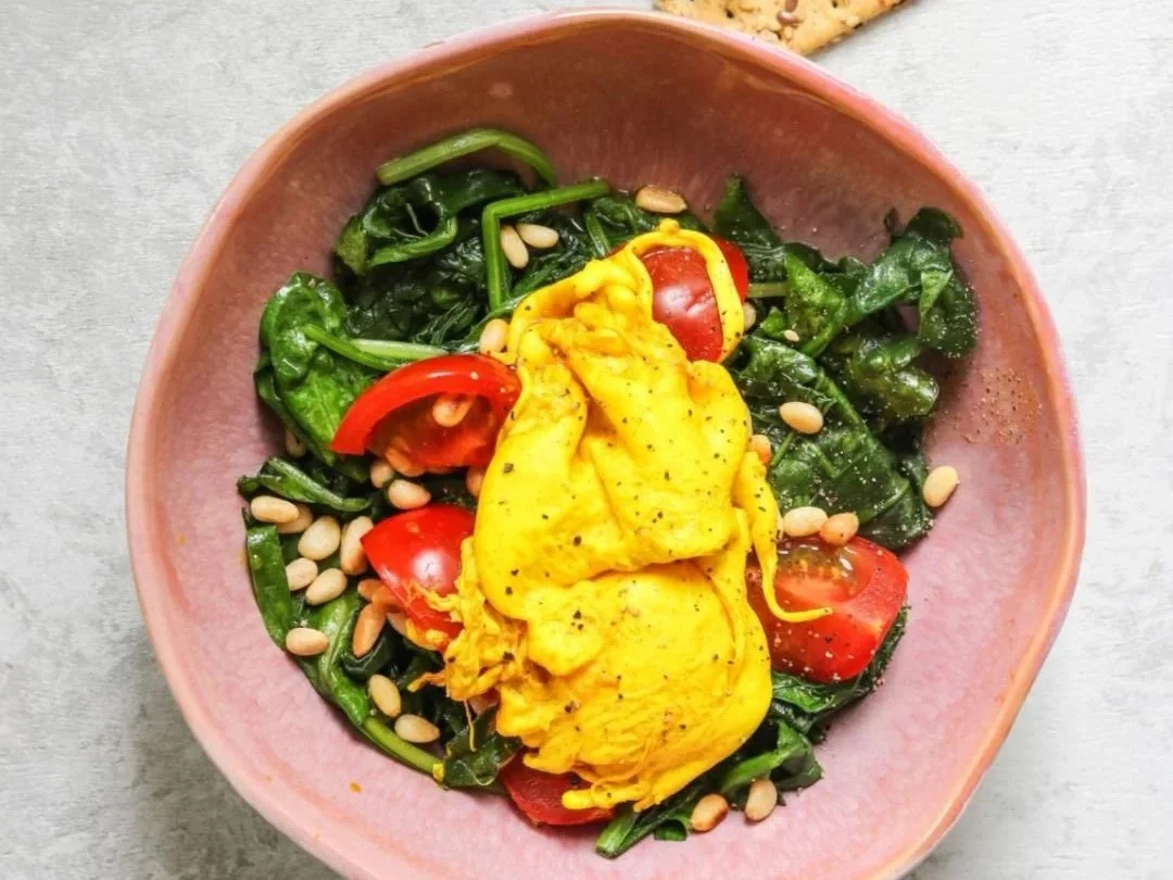 Poached eggs with golden yolks over wilted spinach and tomatoes