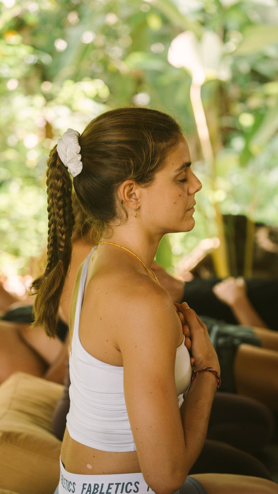 Woman meditating with eyes closed, seated in a serene, natural environment with lush green background.