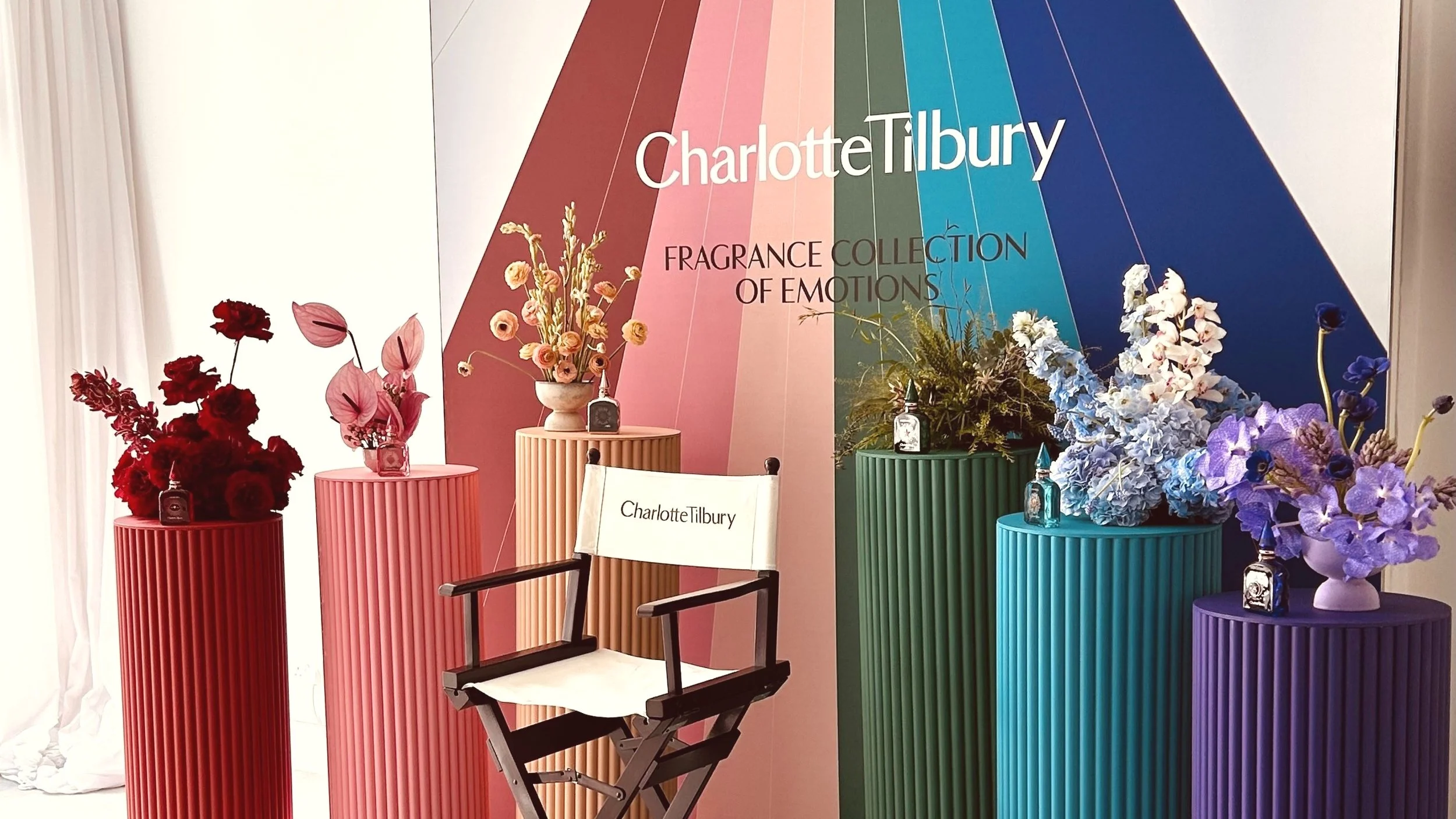 Display of colorful flower arrangements on tall, ribbed pedestals at a Charlotte Tilbury fragrance event.