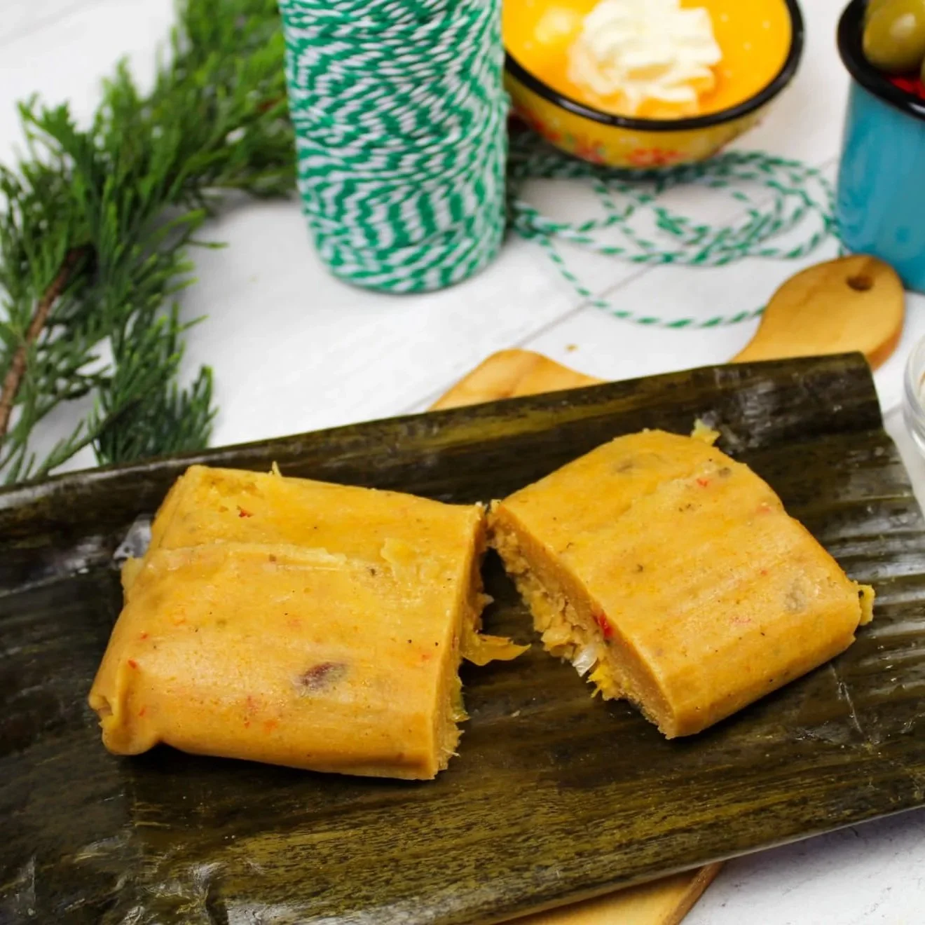 Venezuelan Christmas bollo shown on plantain leaf with olives, cheese and string in background