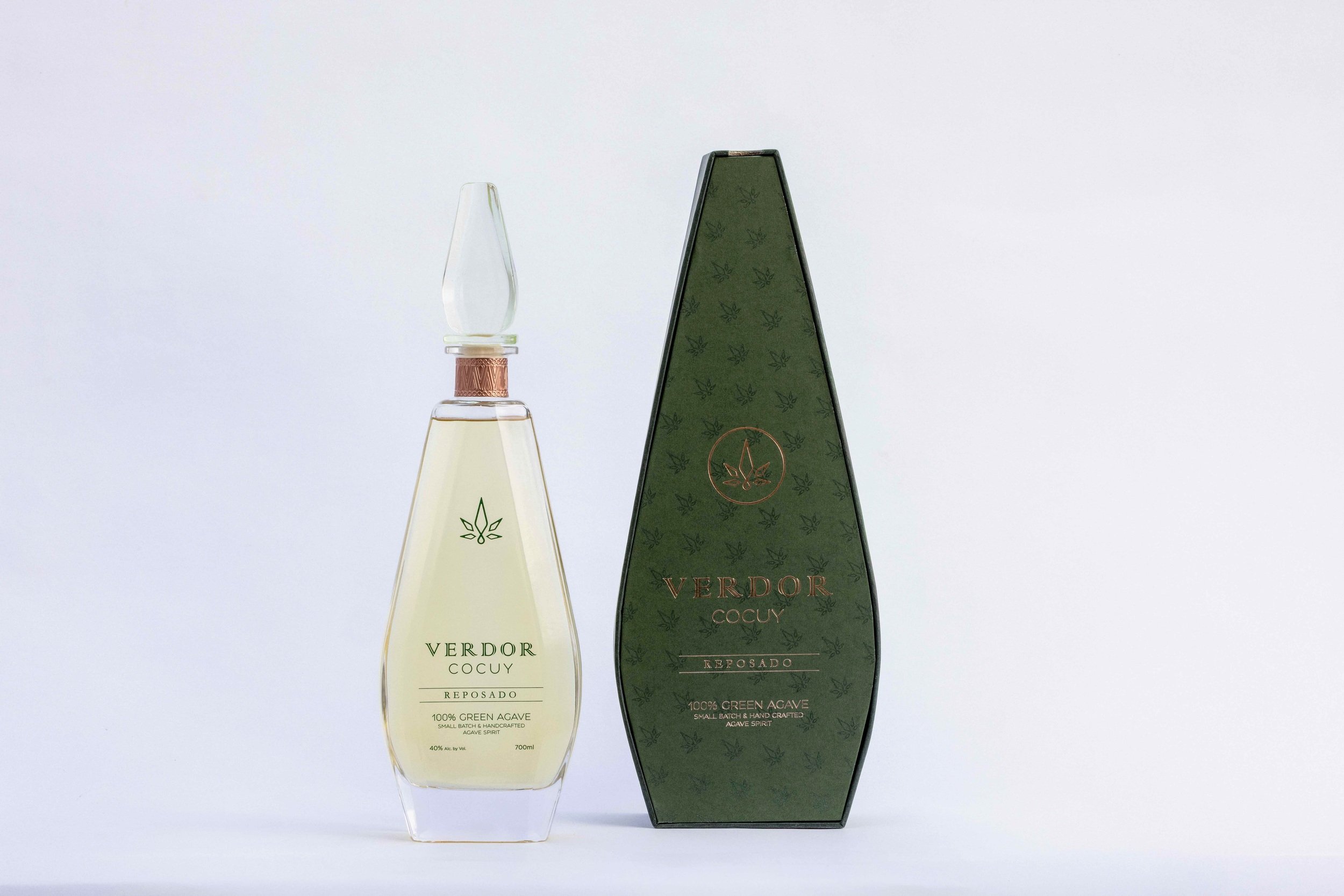 Clear Glass bottle with gloden liquor inside. Diamond shape lid with green logo name standing in a whithe background next to a dark green elegant and magnetic closing box