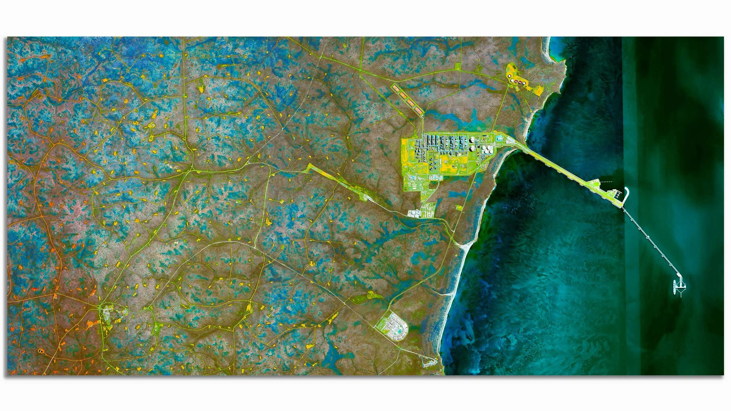 Satellite view of a coastal area with a long bridge extending into the water, industrial facilities near the shoreline, and a network of roads and wetlands inland.