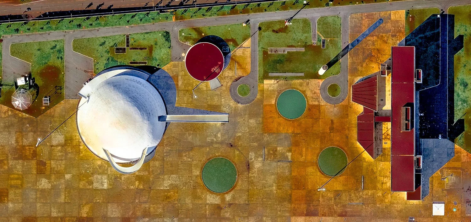 Aerial view of an industrial facility or plant with large storage tanks, pipelines, and buildings on a paved surface.