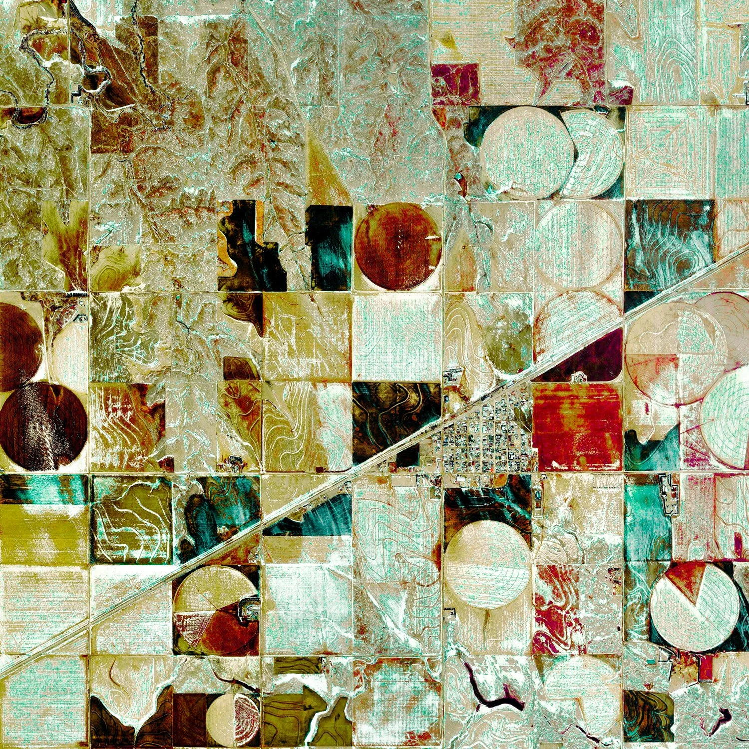 An aerial view of an agricultural landscape with various fields of different shapes, sizes, and colors including green, brown, and red. The fields are separated by roads and irrigation channels, with some circular and rectangular patterns visible.