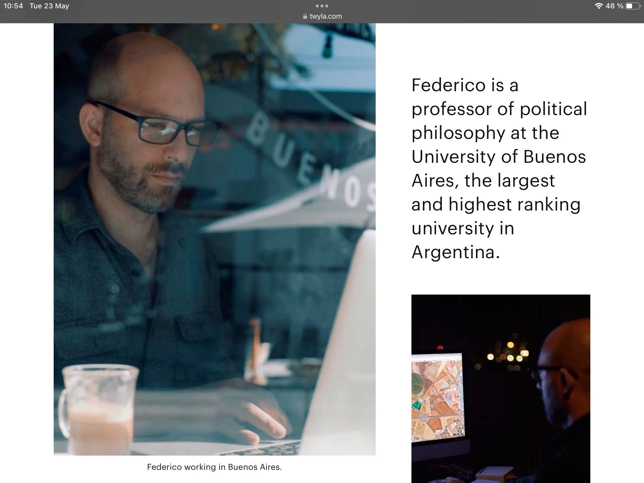 A man with glasses and a beard working on a laptop in Buenos Aires, with a glass of iced coffee on the desk.