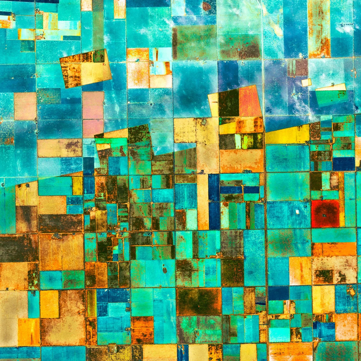 Colorful aerial view of farmland with various rectangular and square fields in shades of blue, yellow, orange, and green.
