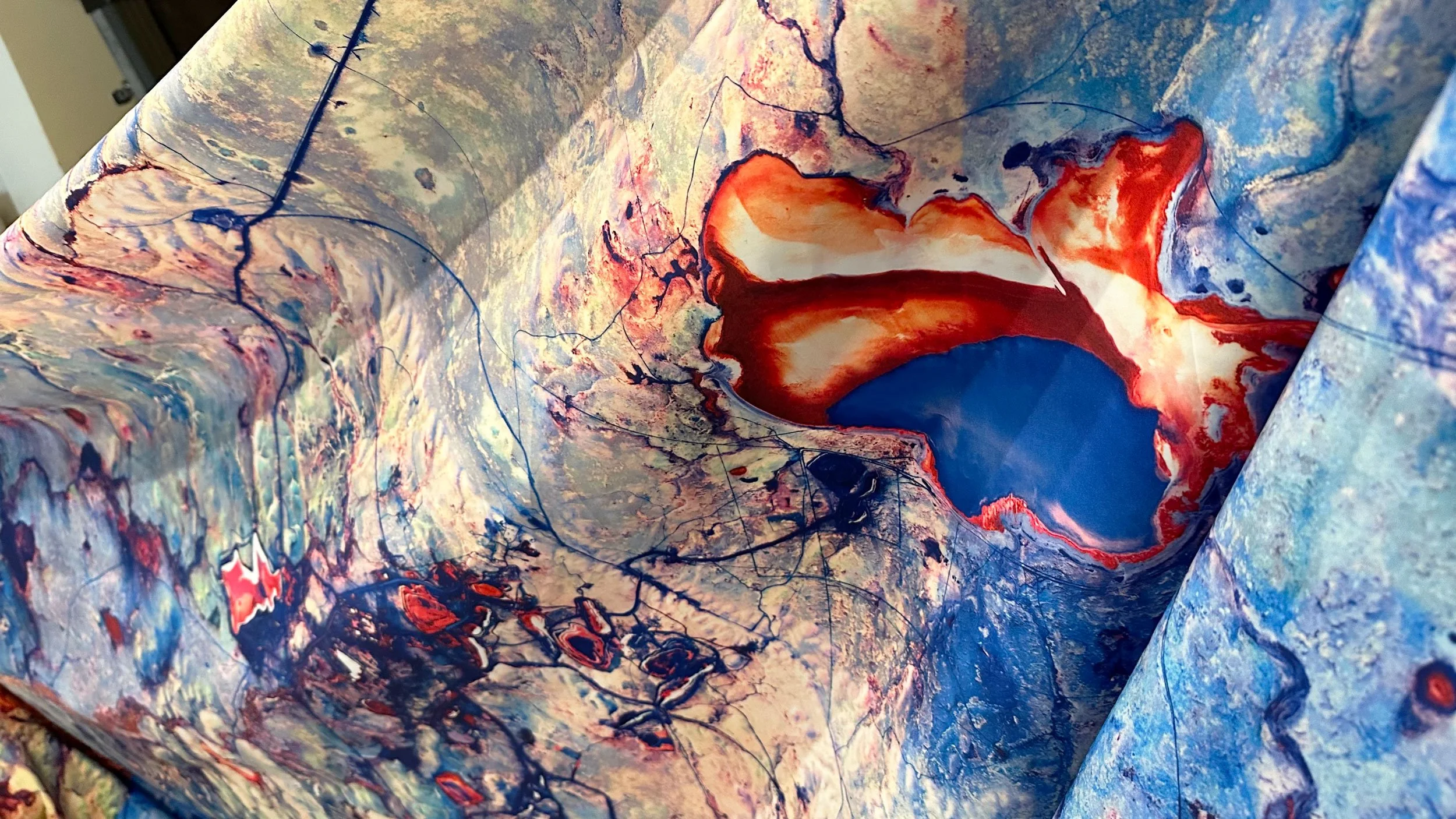 Abstract fluid art painting with swirling patterns and vibrant colors including red, orange, blue, beige, and black, creating a dynamic and textured visual effect.