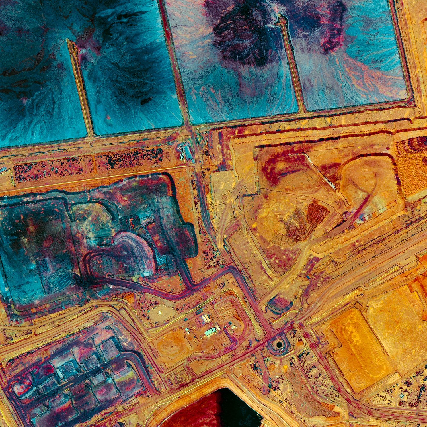 Aerial view of an open-pit mining site with terraced excavation levels, several small water ponds, and surrounding roads and patches of green vegetation.