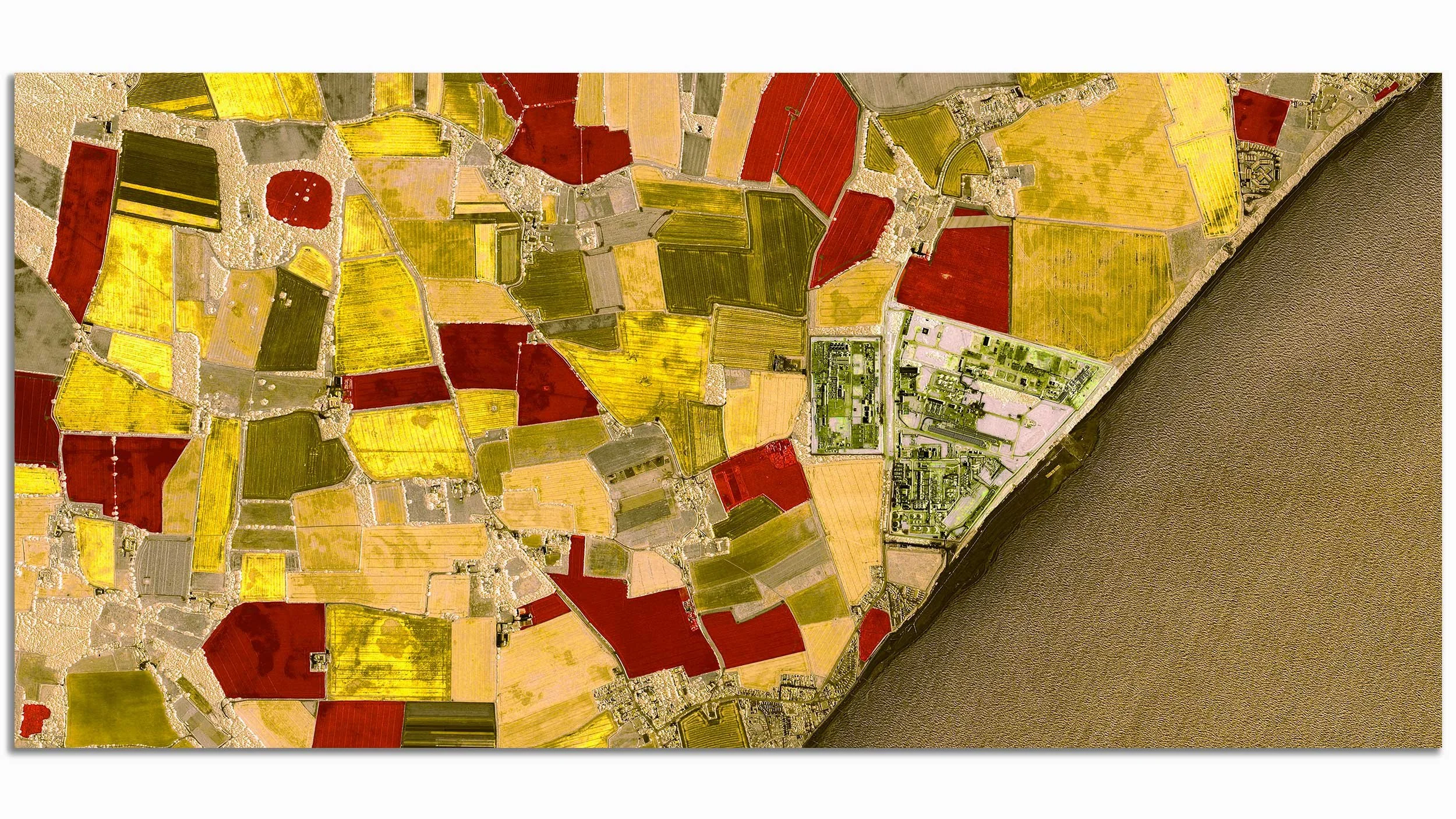 Aerial view of farmland with various colored fields near a river, featuring patches of yellow, red, green, and brown.