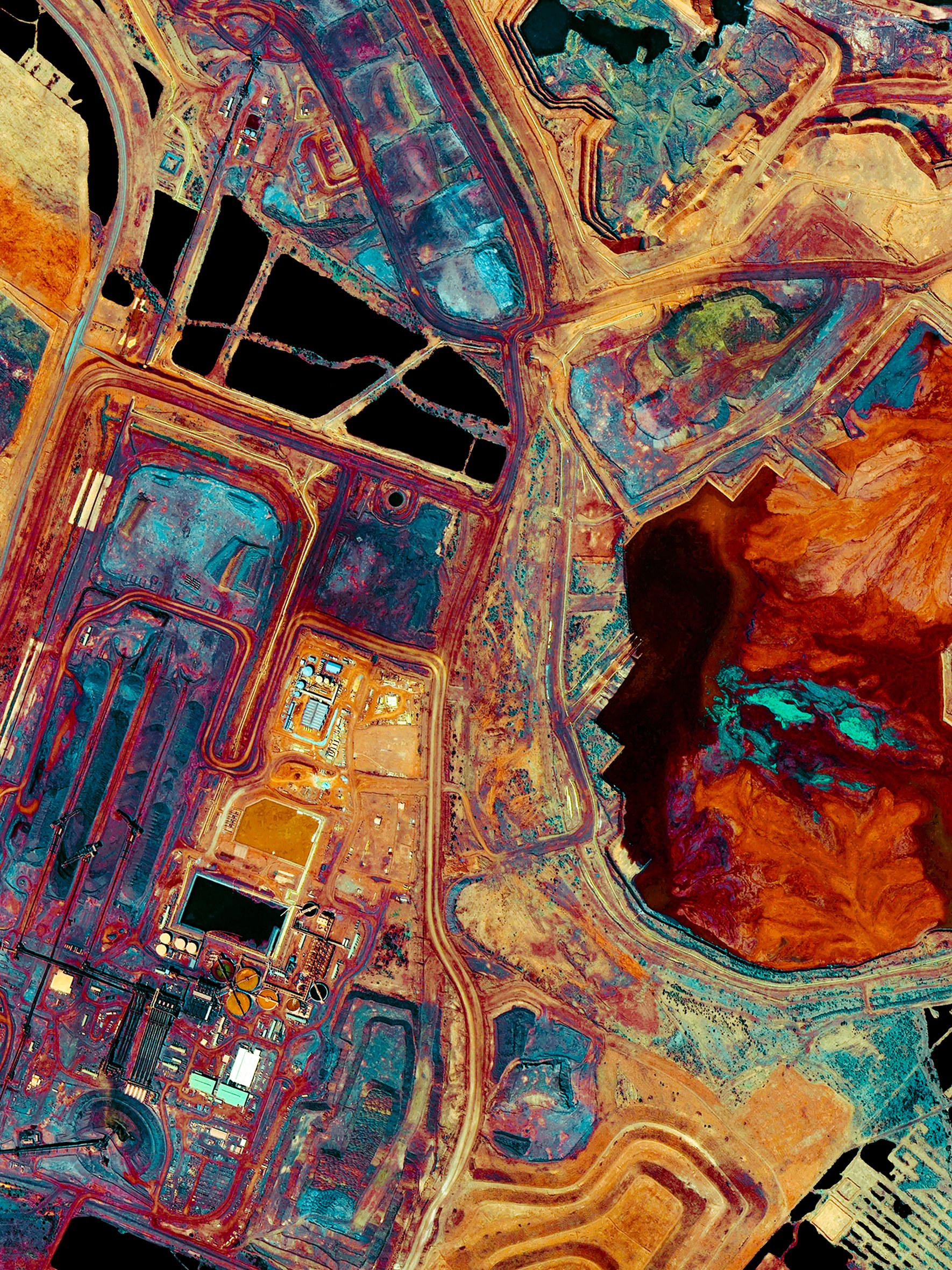 Aerial view of a mining dam with colorful water, surrounding land, and some clouds overhead.