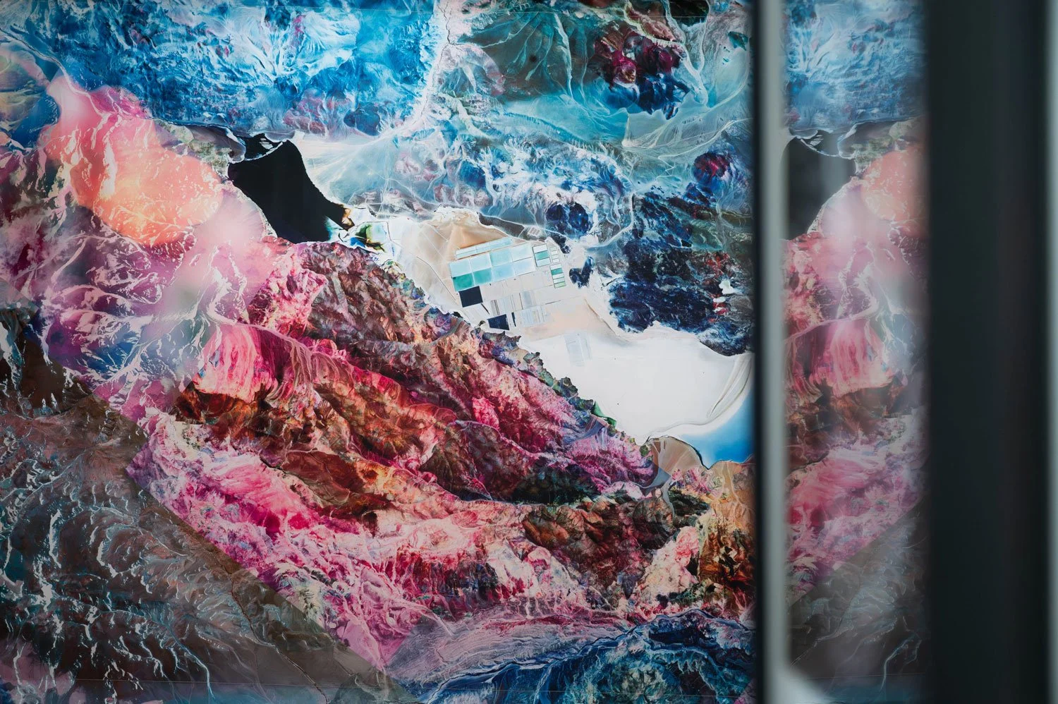 Colorful aerial view of mountains, lakes, and desert landscape viewed through a window.