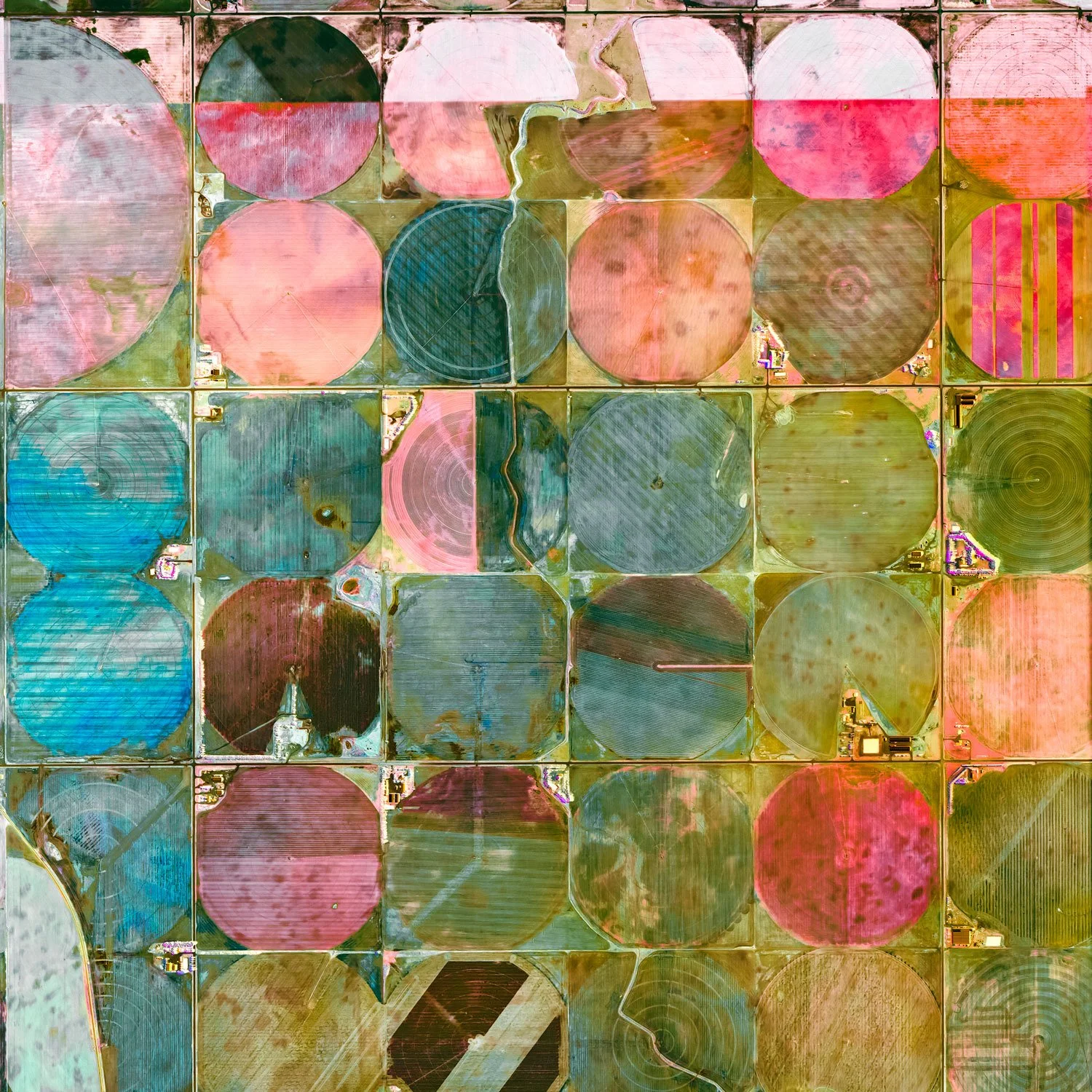 Aerial view of farmland with large circular crop fields in various colors, separated by roads and irrigation canals.