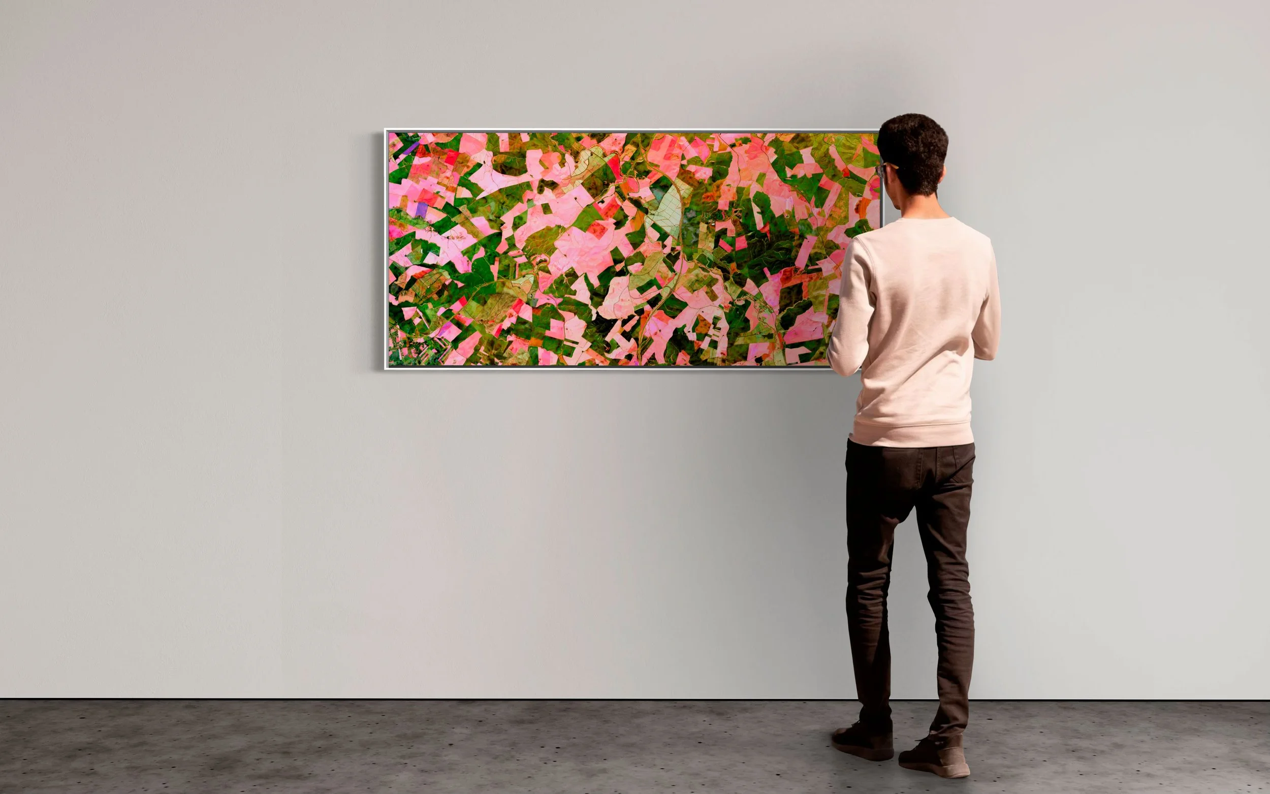 Museum installation of High-resolution satellite view of agricultural fields in Córdoba, Andalusia, Spain, showing irregular plots in pink, green, and earthy tones forming an organic patchwork landscape with roads and natural boundaries.