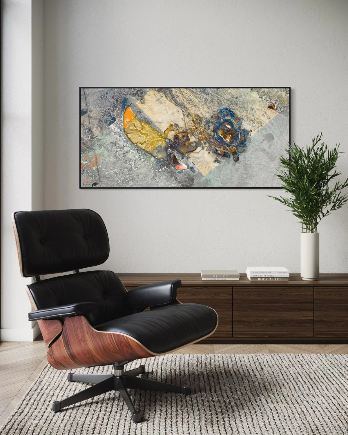 Modern office with black leather lounge chair, wood sideboard with books and a white vase with green plant, framed abstract art on white wall.